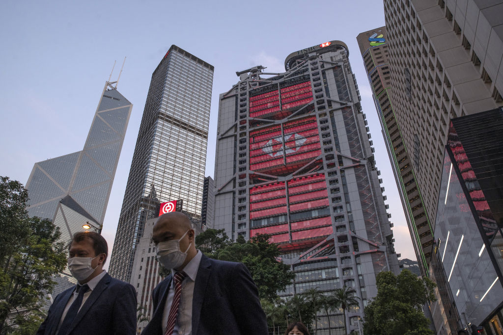 Pedestrians wearing protective masks walk as the HSBC Holdings Plc headquarters building, center, stands illuminated in the Central district of Hong Kong, China, on Monday, April 27, 2020. (Roy Liu/Bloomberg via Getty Images)