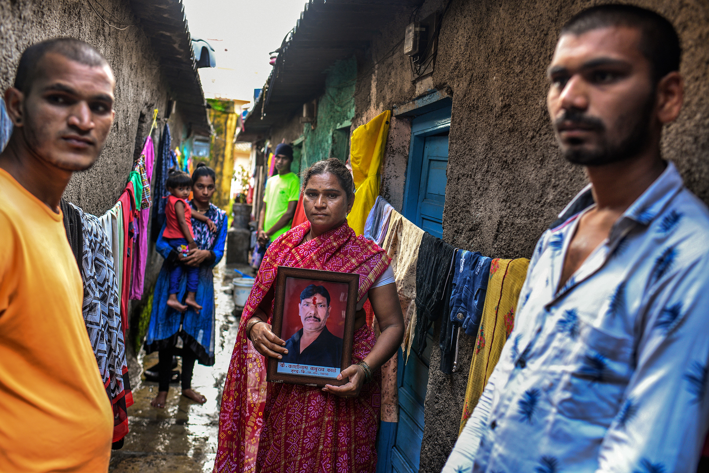 Kashinath Kale's widow, Sangeeta, flanked by her sons Akshay, left, and Avinash, holds a framed portrait of her late husband outside their home in Kalewadi, a suburb of Pune. Kale, 44, died from COVID-19 in July as the family desperately tried to find a hospital bed with a ventilator.