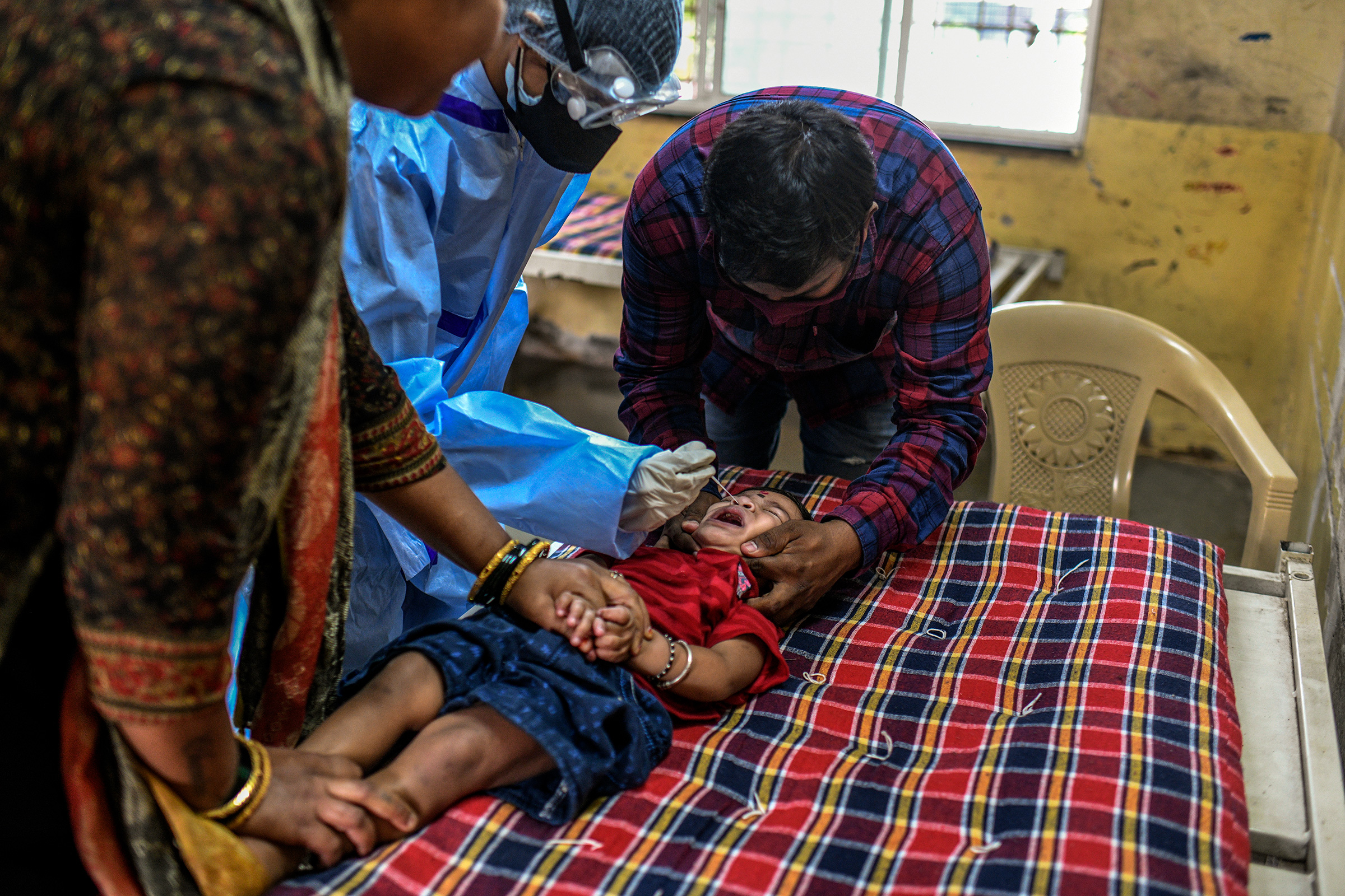 Los padres mantienen a sus hijos tranquilos mientras un trabajador de la salud toma un hisopo nasal para una prueba de COVID-19 en una escuela en Pune.