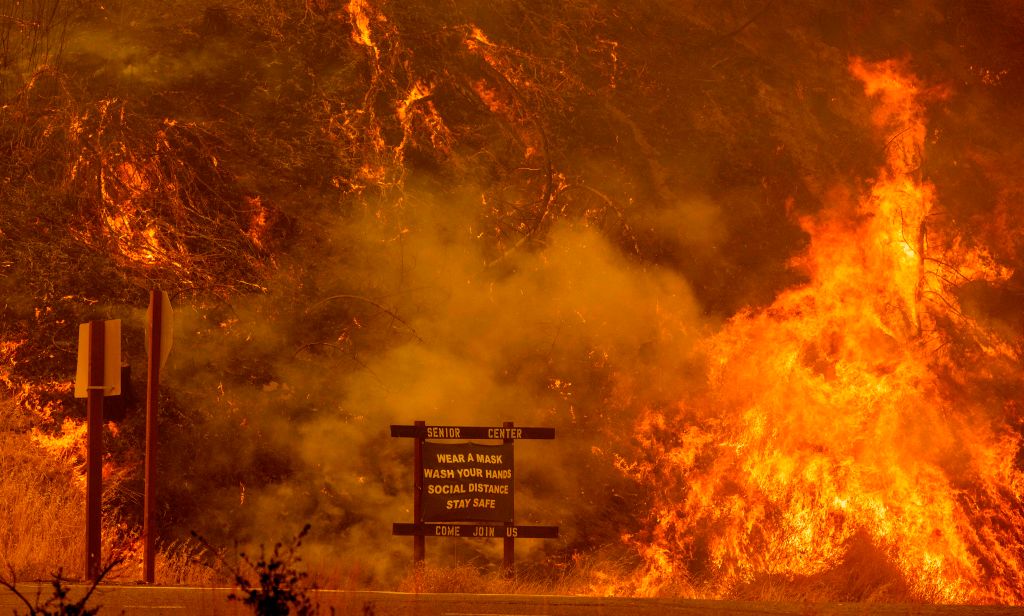 A sign warning people about COVID-19 is surrounded by flames during the Hennessey fire on Aug. 18, 2020, near Lake Berryessa in Napa, Calif. (Josh Edelson—AFP/ Getty Images)
