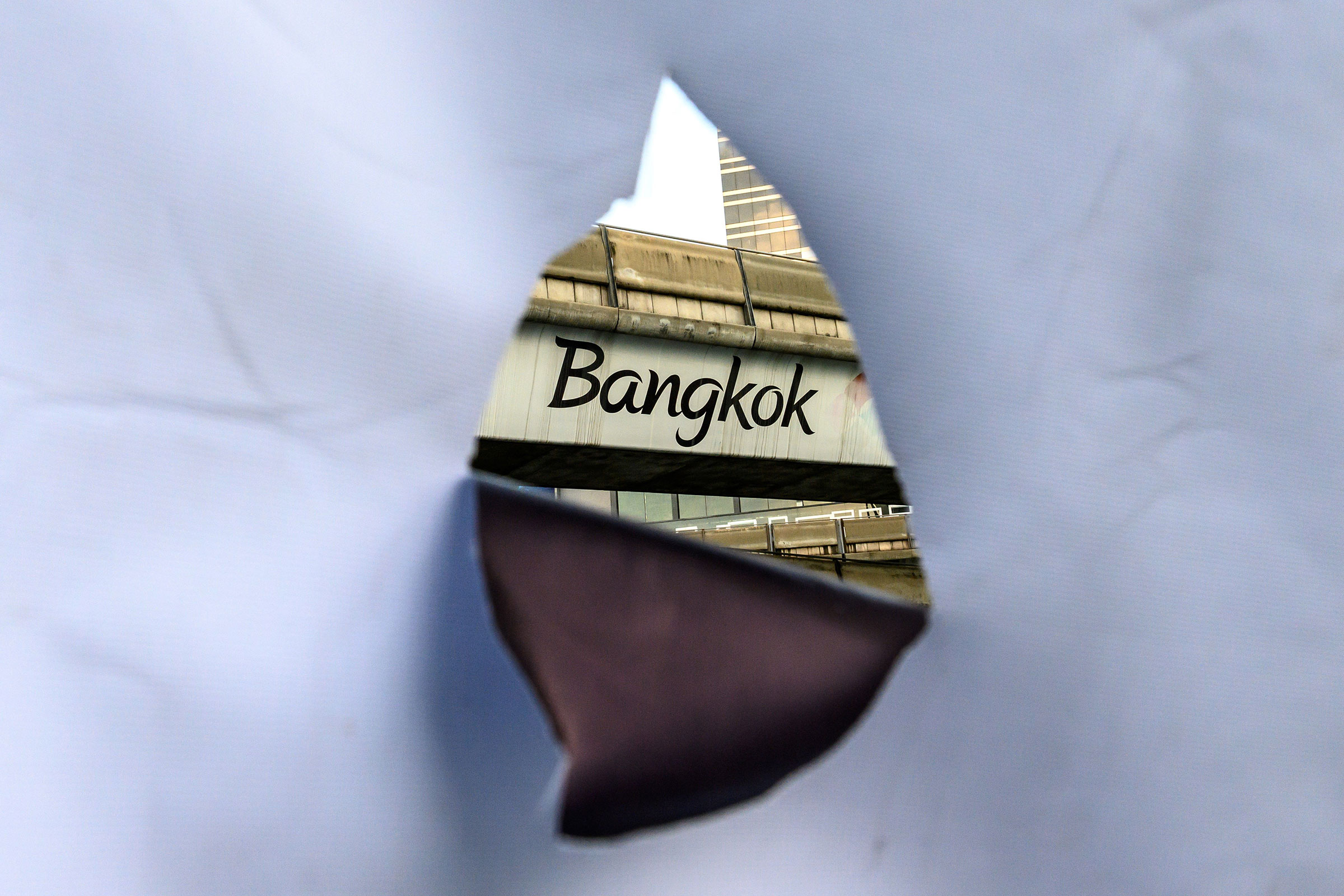 A Bangkok inscription on a sky train bridge is seen through the hole of a banner
