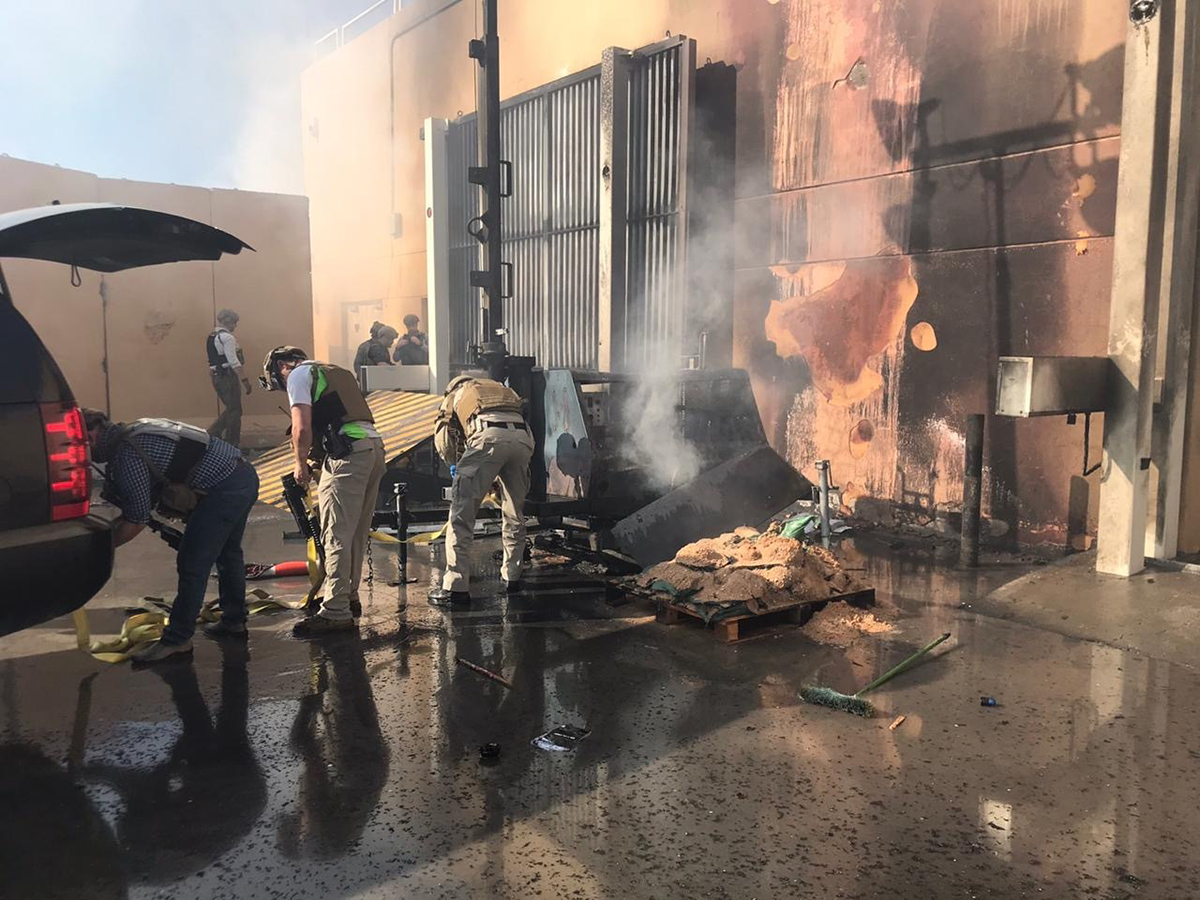 Special Agent Evan Tsurumi, front-center, helps to remove a burning obstacle during an attack on the U.S. embassy in Baghdad. In the background, DSS Special Agent Mike Yohey and others examine ways to barricade an entrance at the embassy.