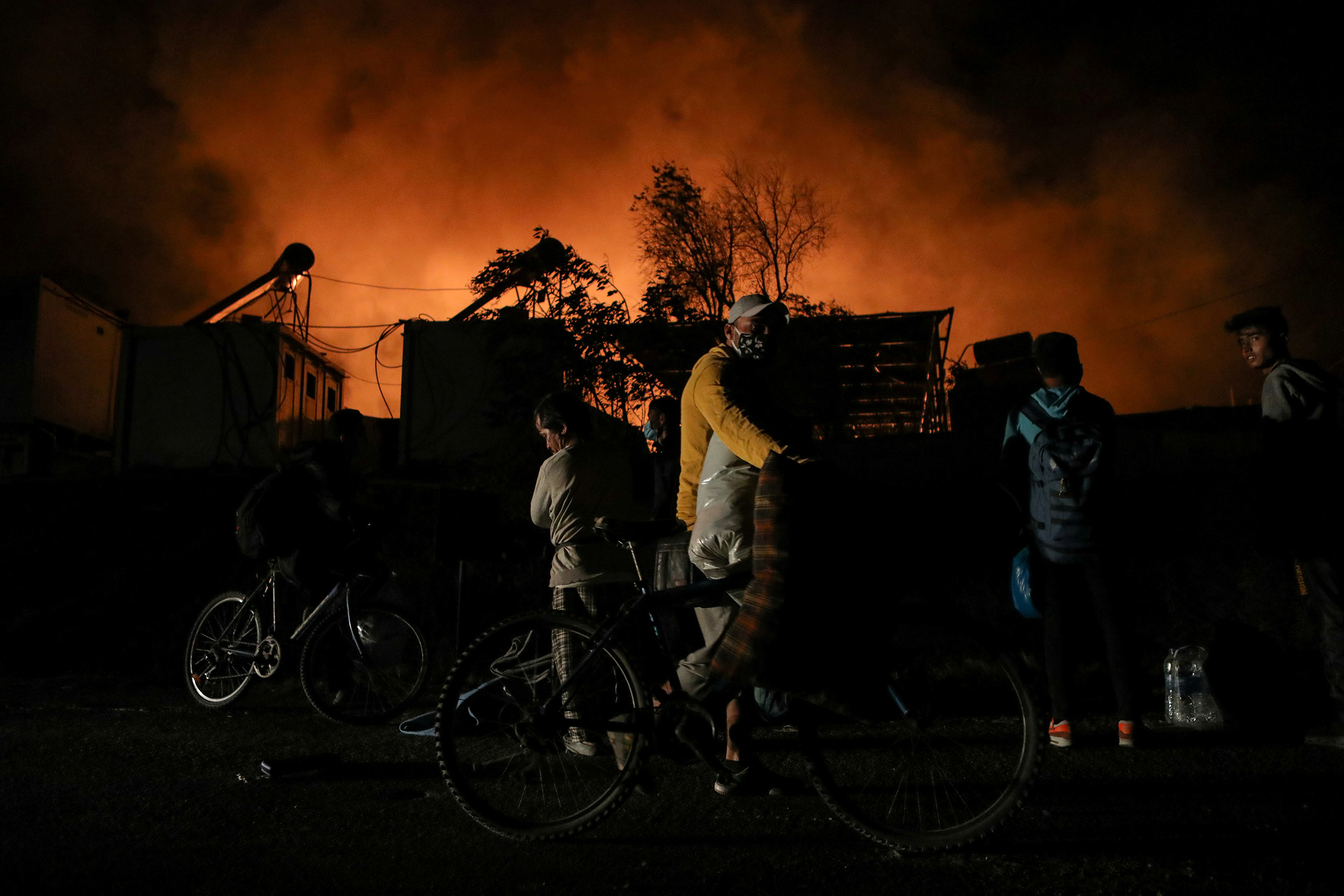 Refugees and migrants carry their belongings as they flee from a fire burning at the Moria camp on the island of Lesbos, Greece, on Sept. 9, 2020. (Elias Marcou—Reuters)