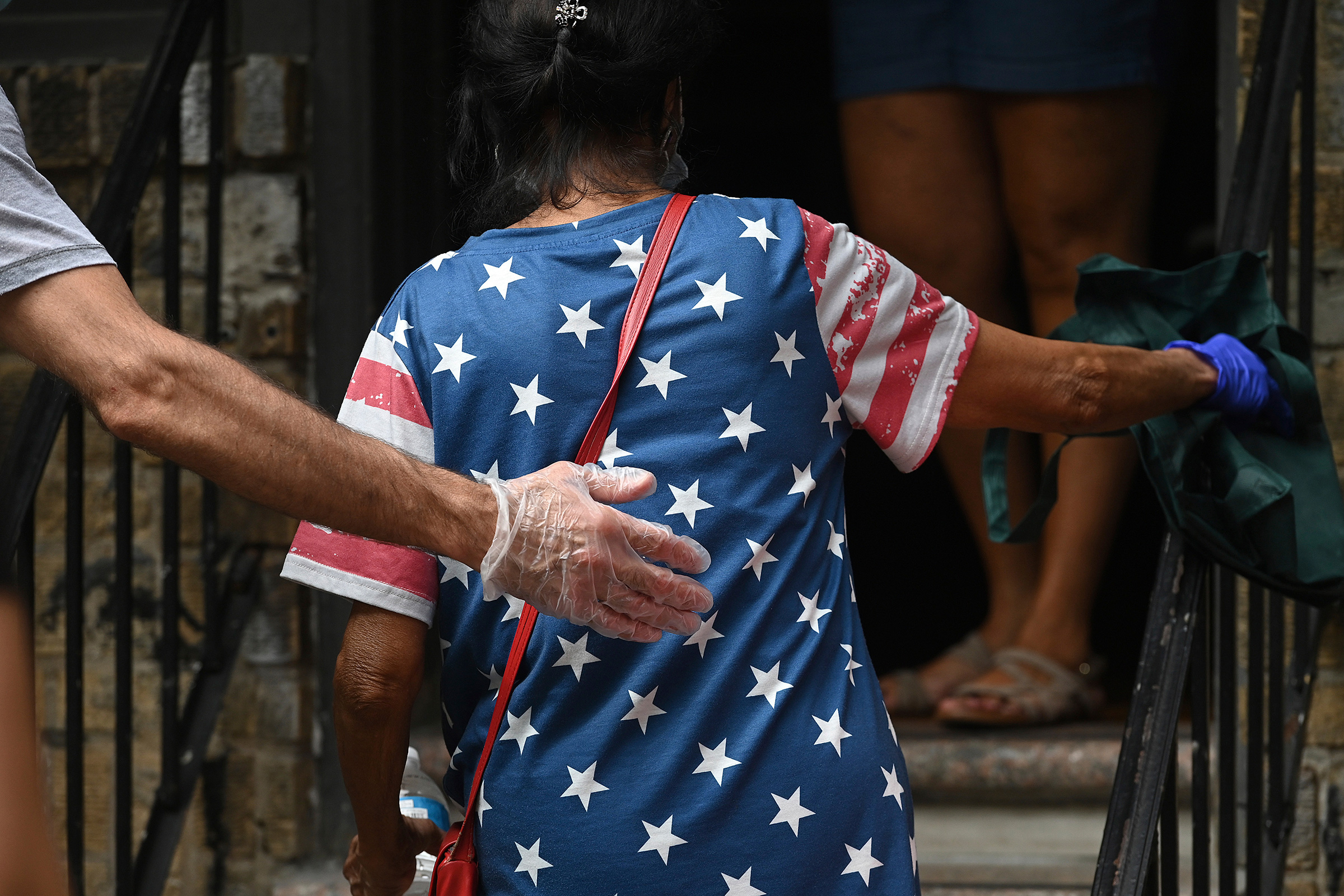 With an outstretched gloved hand, a volunteer helps a woman up the steps of the Mosaic Community Center Food Pantry to receive donated food in Queens on July 31 (Anthony Behar—Sipa USA/AP)