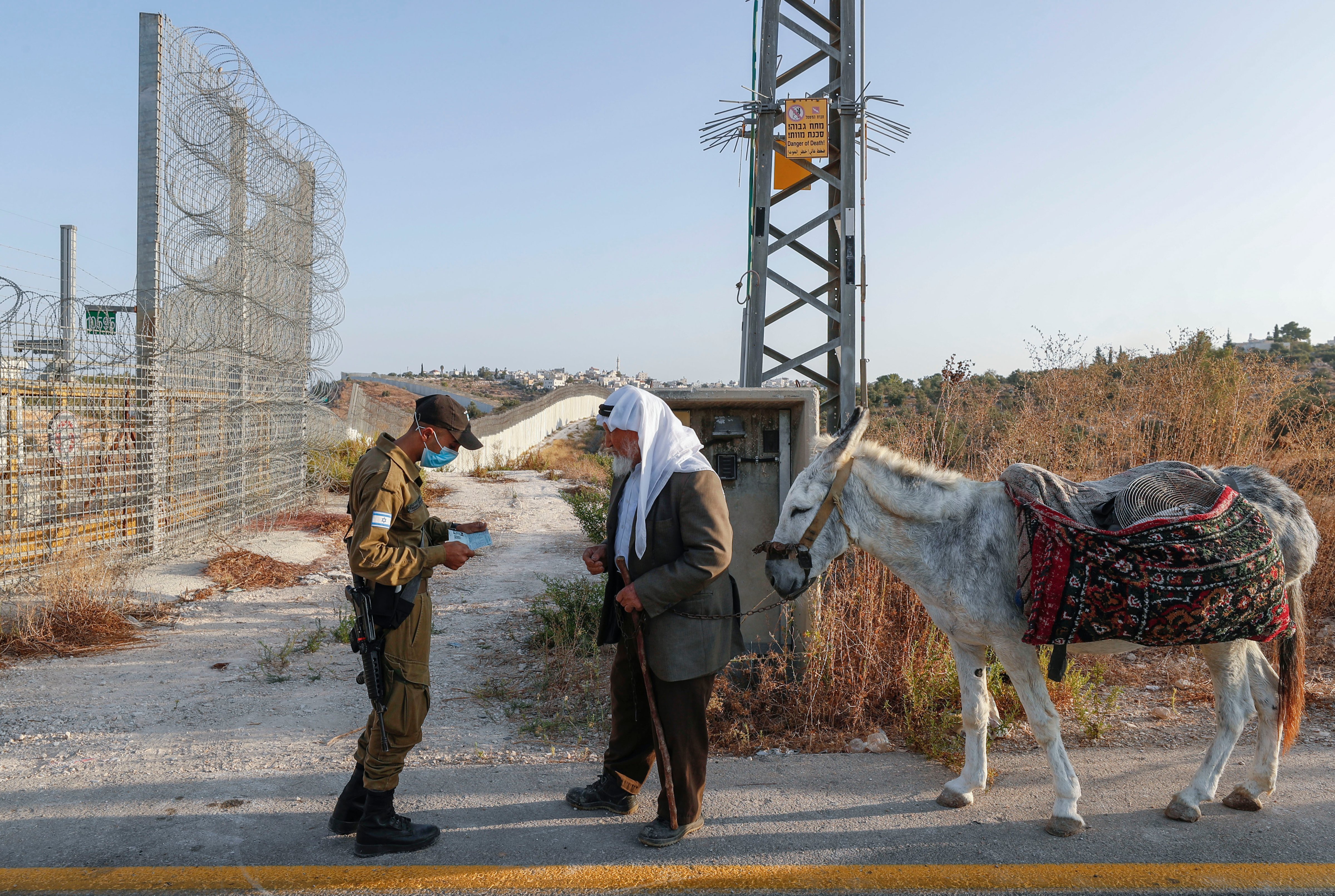 An Israeli soldier checks the authorisation of a Palestinian man taking his donkey to harvest olives on his land, which was divided by Israel's controversial separation barrier, near the West Bank village of Bayt Awwa, on October 12, 2020. (Emmanuel Dunand—AFP /Getty Images)