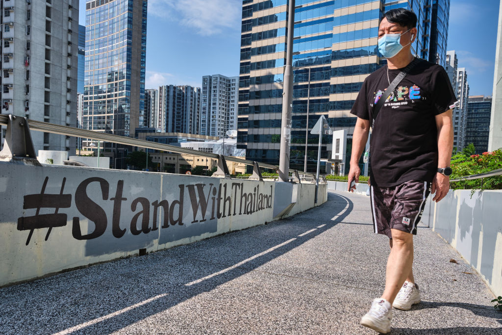 A man wearing a facemask walks past a "#StandWithThailand"