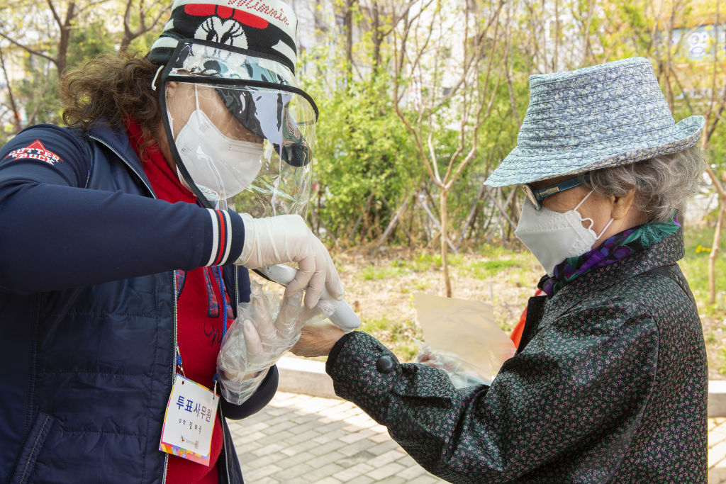 A poll worker wearing a medical mask and plastic gloves checks the body temperature of a citizen South Korean citizen, at a polling station at the country's general election amid the coronavirus outbreak in Seoul on April 15, 2020. (Jong Hyun –Anadolu Agency/Getty Images)
