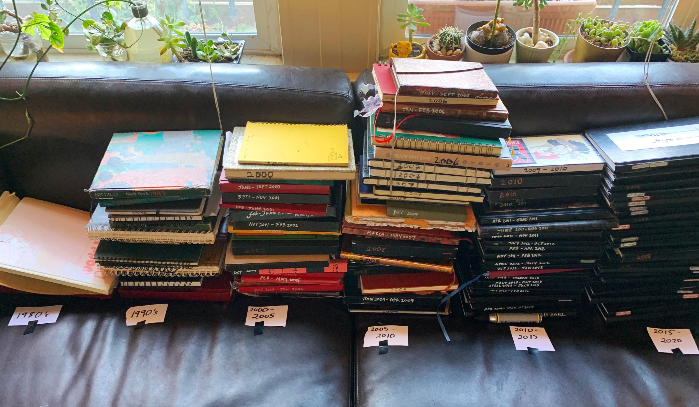 Multiple stacks of Nayomi Munaweera's journals separated by decades lying on her couch