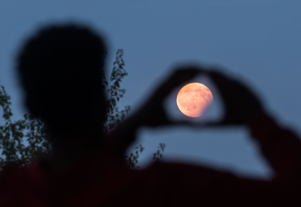 A man frames with his hands the moon standing in a partial lunar eclipse on August 7, 2017 in Frankfurt am Main, western Germany. (Frank Rumpenhorst—DPA/AFP/Getty Images))