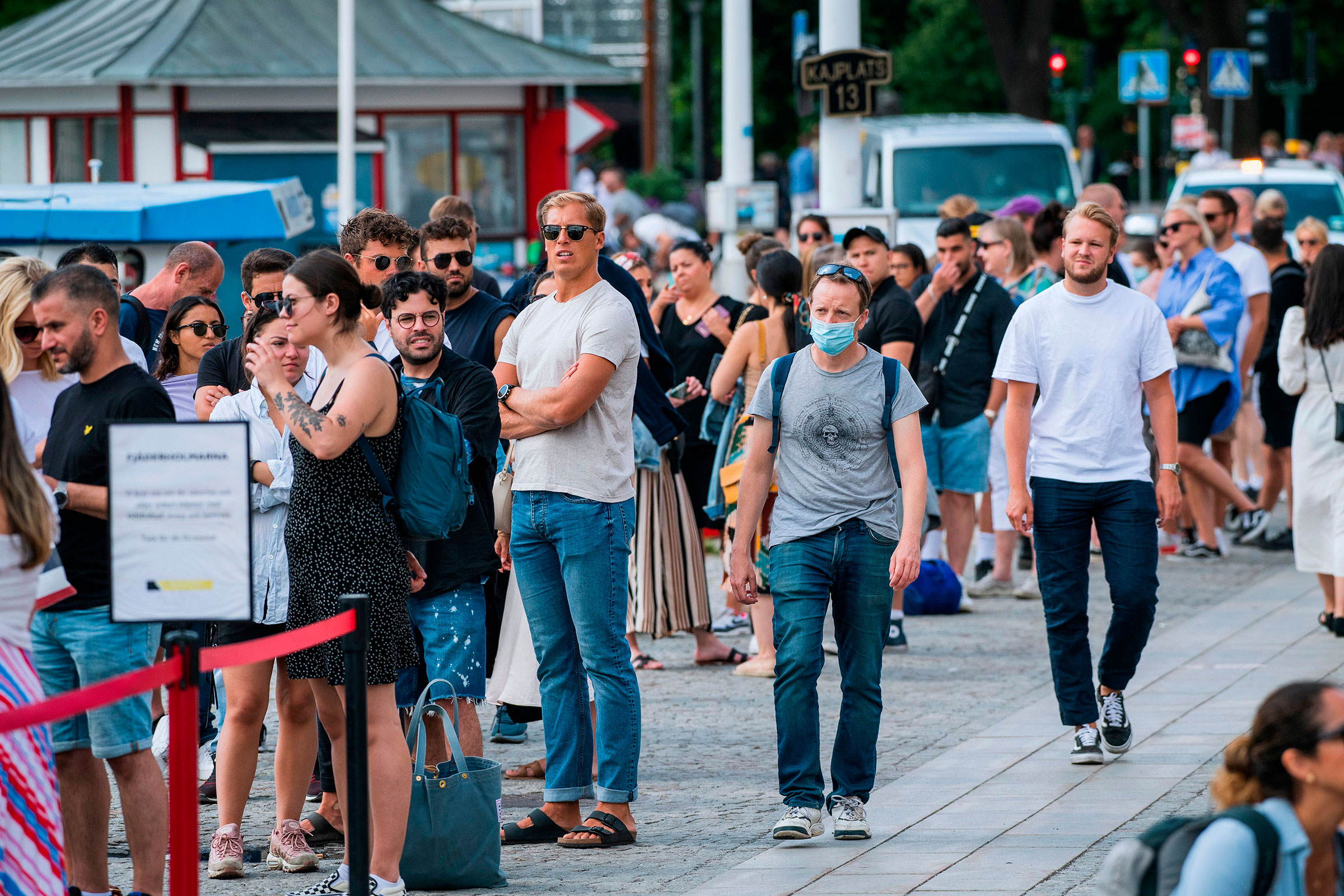 A man wearing a protective mask walks next to travelers as they queue up to board a boat in Stockholm on July 27, 2020. (Jonathan Nackstrand—AFP/Getty Images)