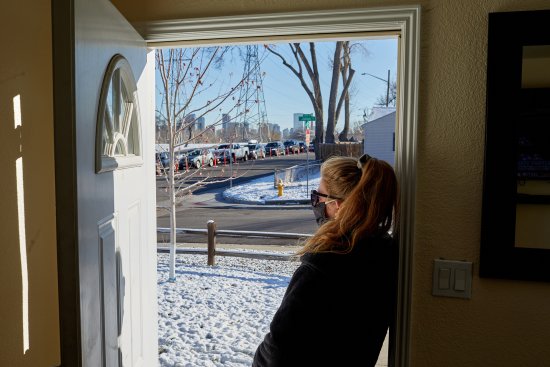 A Denver woman looks out from her home, on Nov. 10., at a line of cars with people waiting to get tested for COVID-19