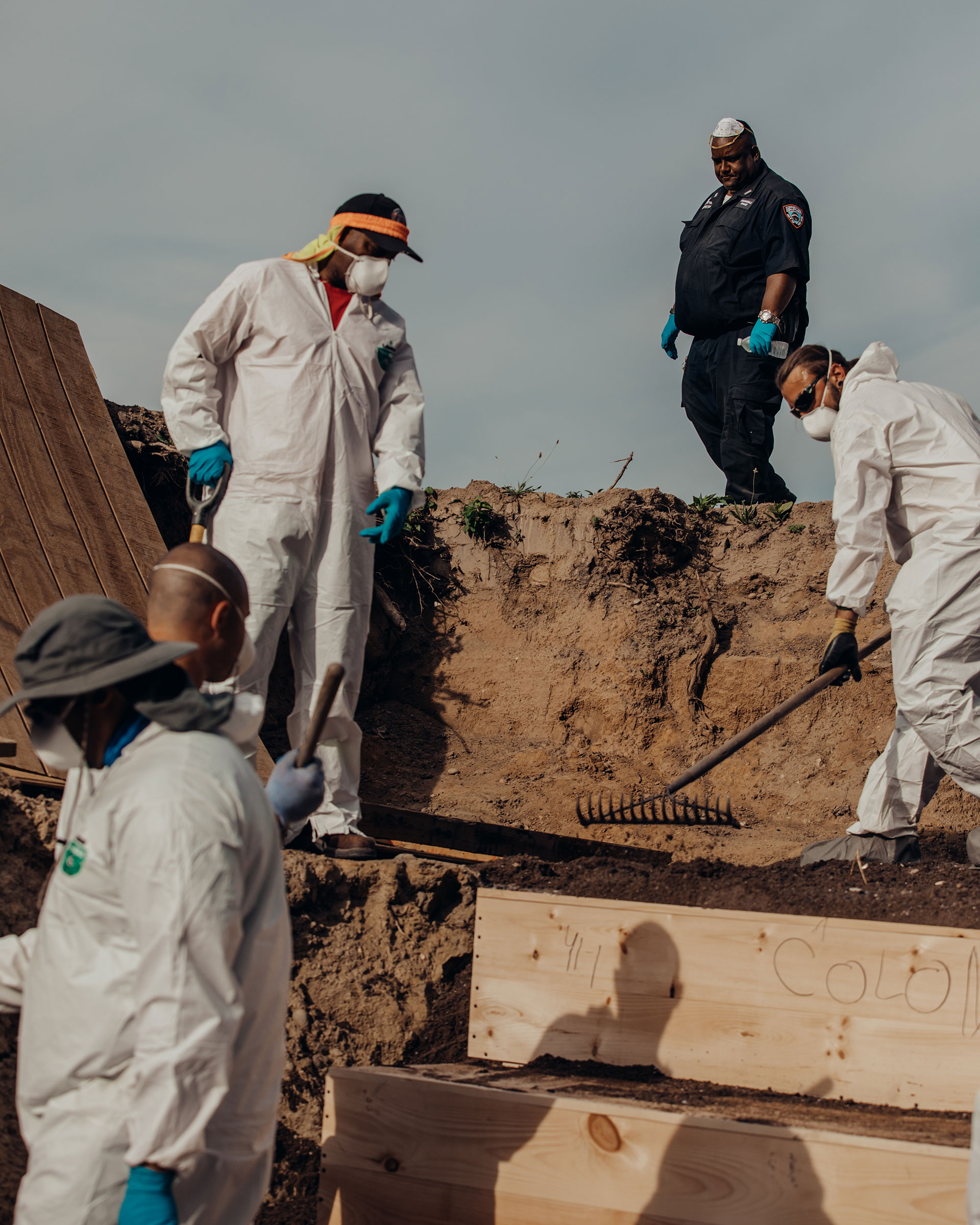 Workers place pine caskets inside a mass grave on Hart Island while correction officers look on. (Sasha Arutyunova for TIME)