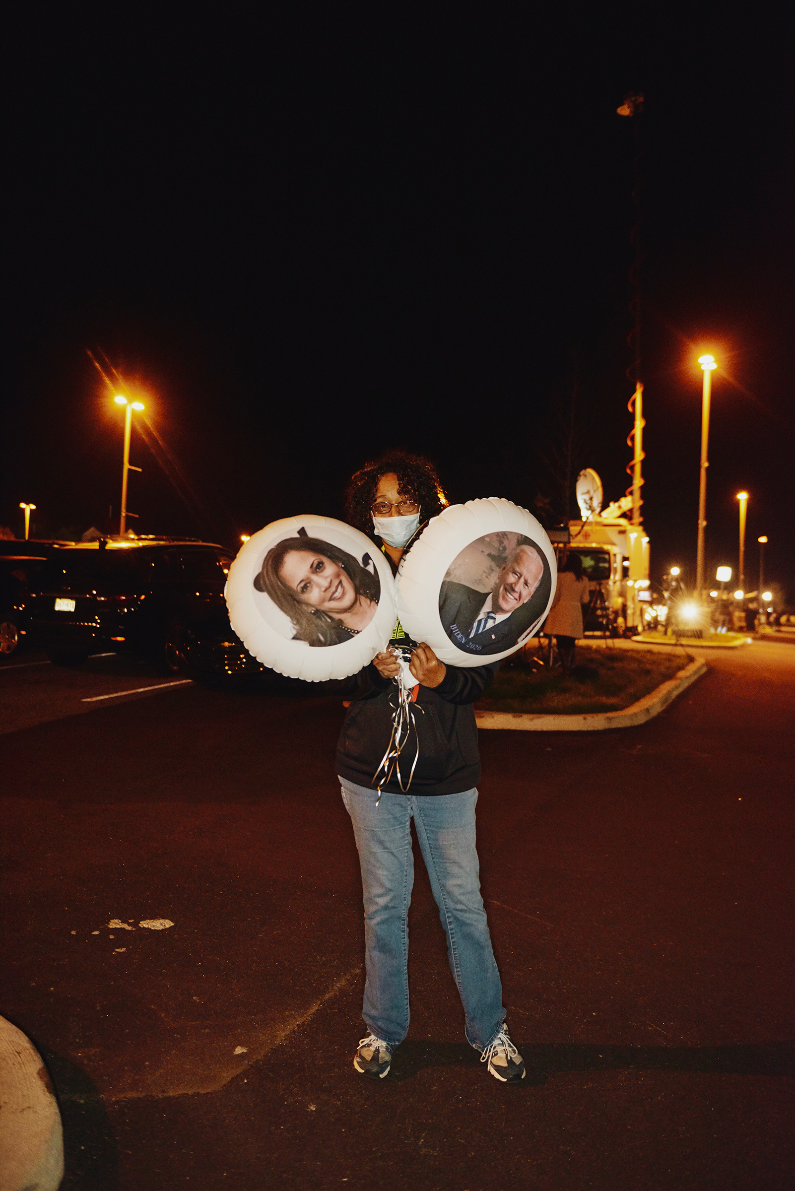 Violetta Smith holds portrait balloons of Harris and Biden at an outdoor election-night event in Wilmington, Del.