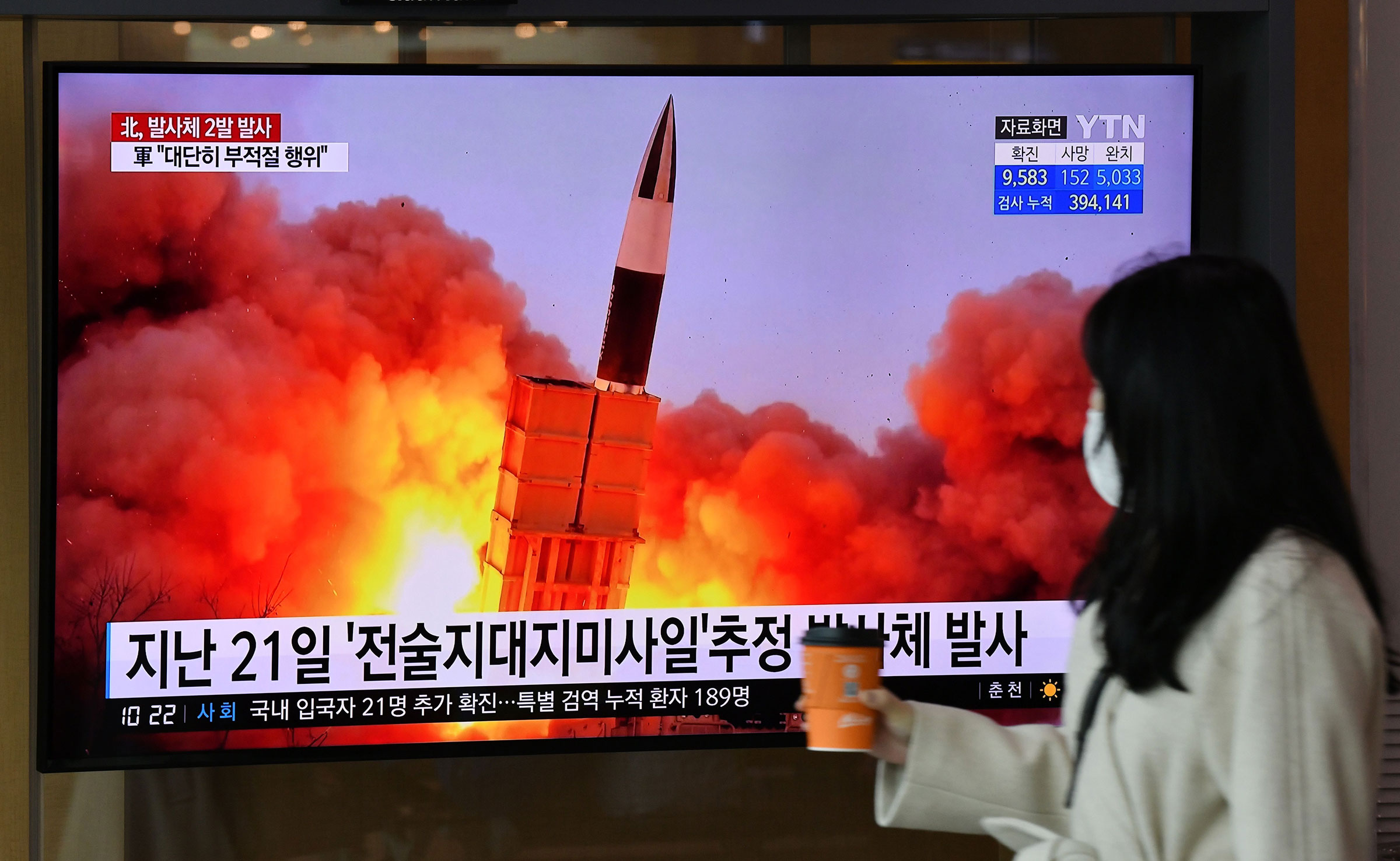 A woman walks past a screen showing file footage of a North Korean missile test, at a railway station in Seoul on March 29