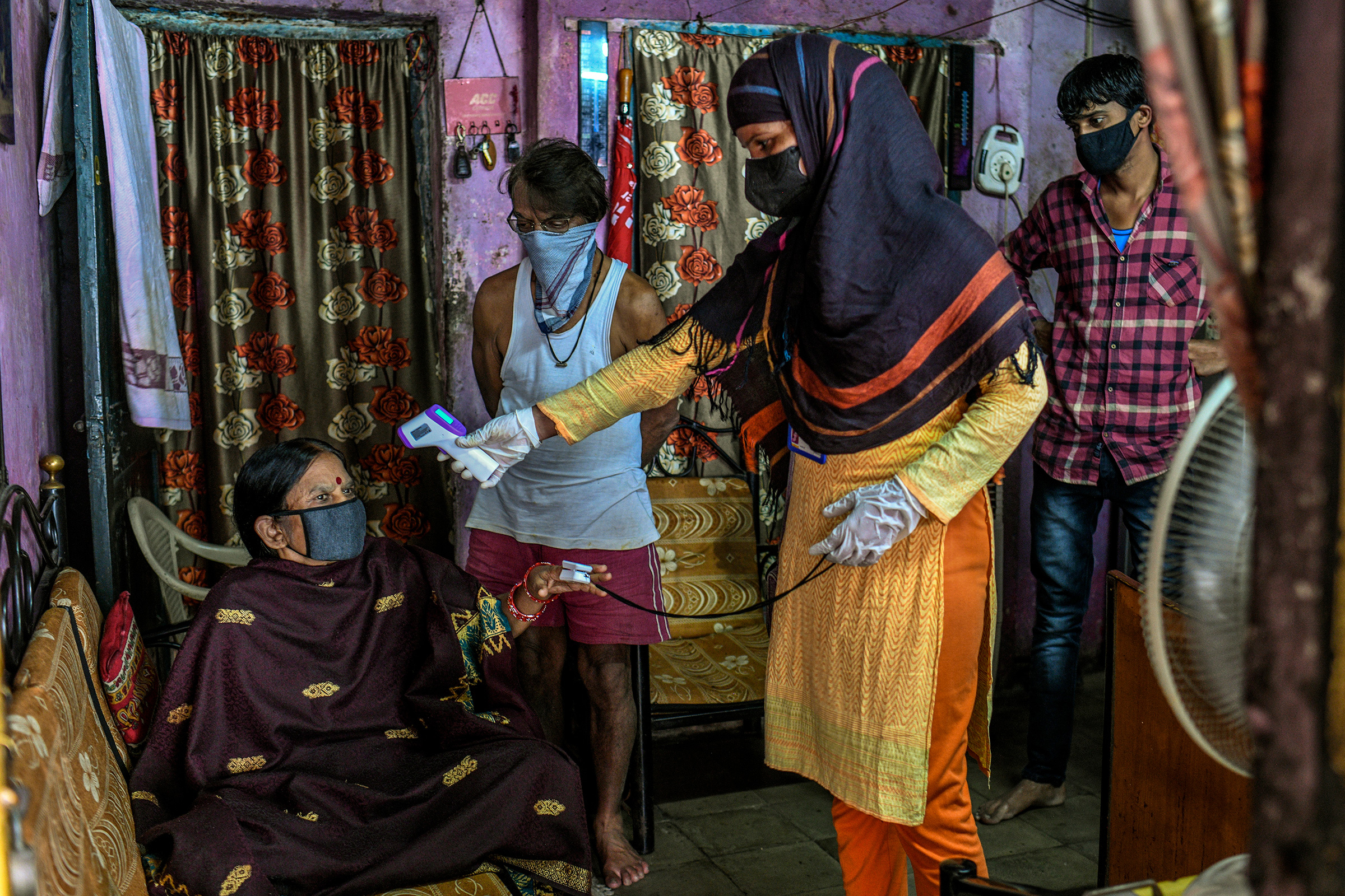A health care worker checks a woman's temperature and oxygen saturation in the Dhole Patil slum of Pune, India, on Aug. 10, 2020.