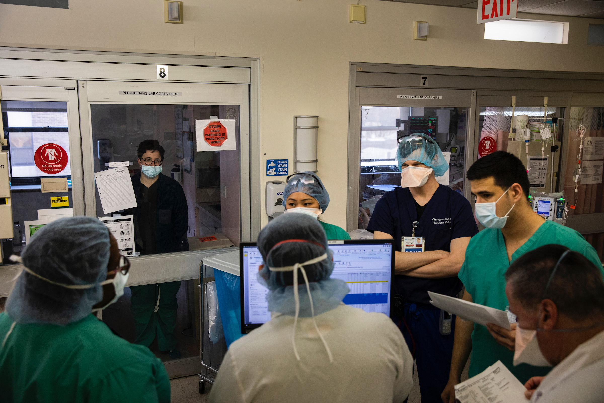 March 26th, 2020—Brooklyn, NY: Scenes from Maimonides Medical Center in Brooklyn, New York. The hospital is currently treating Covid-19 patients in their ER and ICU units, and are preparing for a bigger rush of potential patients. In the ICU—Dr. Laura Mulvey (33), an ER Physician at Maimonides, in her isolation unit after contracting Covid-19. She can be seen frame left while the ICU team holds a meeting in front of her unit. The team meeting was not intentionally held by her unit, it was just happenstance. She is a patient at this time and was not expected to listen.Photograph by Benjamin Norman for TIME