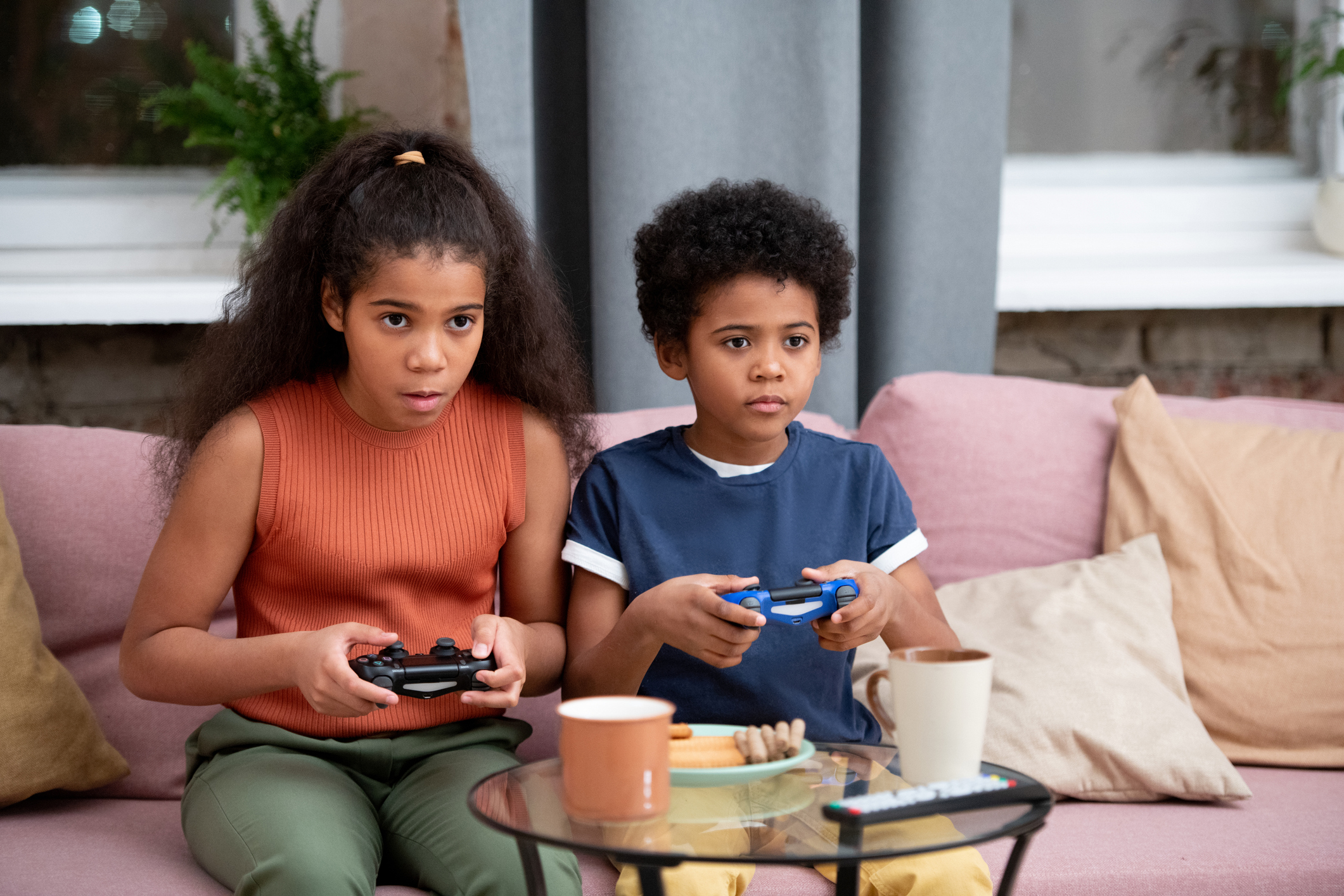Cute boy and girl of African ethnicity playing video game on couch at home