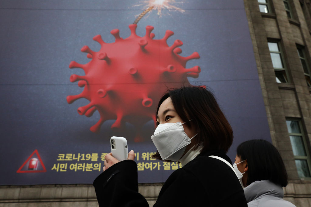 People wearing masks to prevent the spread of COVID-19 walk in front of a banner emphasizing an enhanced social distancing campaign displayed on the wall of Seoul City Hall on November 25, 2020 in Seoul, South Korea. Authorities announced the tightening of social distancing regulations and the closure of some kinds of businesses, including nightclubs, to combat a quickly increase wave of Covid-19 infections this week. (Chung Sung-Jun–Getty Images)