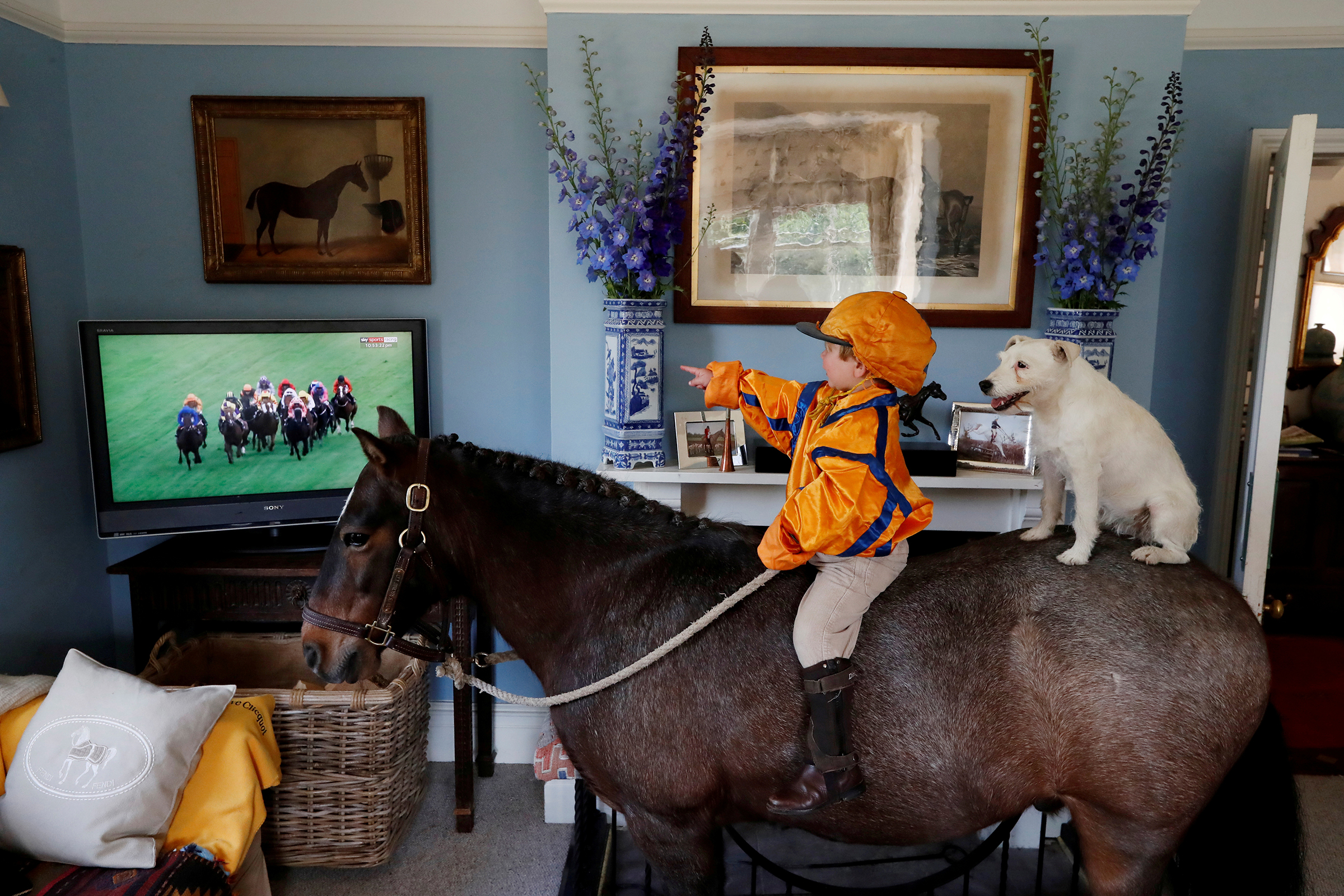Merlin Coles, 3, watches horse racing at Royal Ascot from his home in Bere Regis, Britain, on June 17, 2020. Coles is sitting on his horse, Mr. Glitter Sparkles, with his dog, Mistress, as racing resumed behind closed doors.