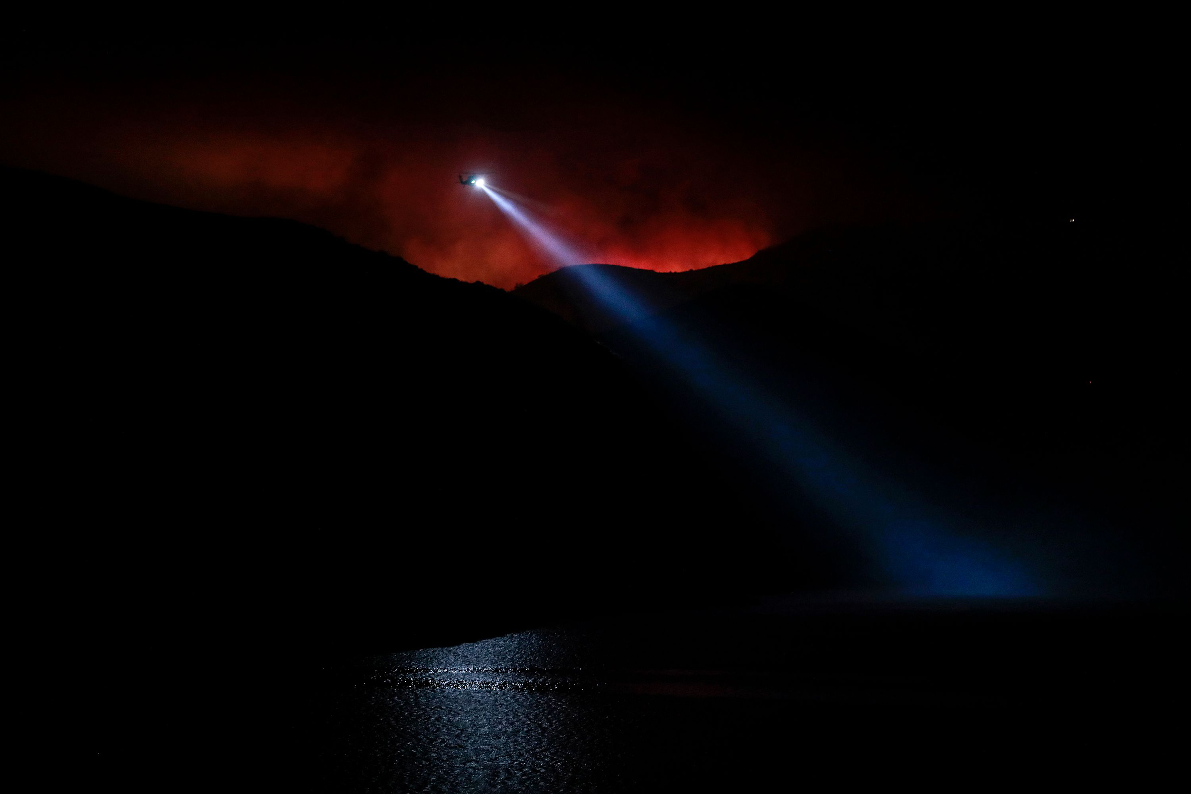 The night sky glows red from the Holser Fire in Piru, Calif., on Aug. 17, 2020, as a water-dropping helicopter works to slow the spread of flames that consumed more than 1,000 acres by the end of its first day just east of Lake Piru.