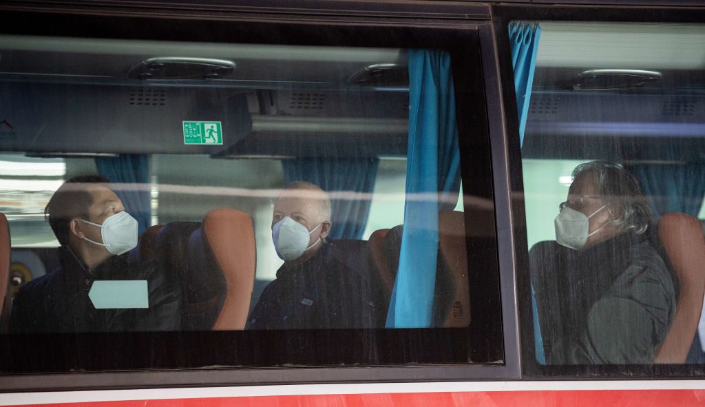 Members of the World Health Organization (WHO) team, including Peter Daszak (C) and Hung Nguyen (L), investigating the origins of the Covid-19 pandemic, board a bus following their arrival at a cordoned-off section in the international arrivals area at the airport in Wuhan on January 14, 2021. (NICOLAS ASFOURI/AFP via Getty Images)