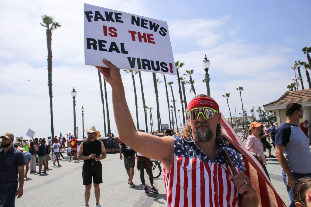 A protester holds a placard that says Fake News Is The Real Virus during a demonstration on May 9, 2020, in California. (Photo by Stanton Sharpe/SOPA Images/LightRocket via Getty Images)