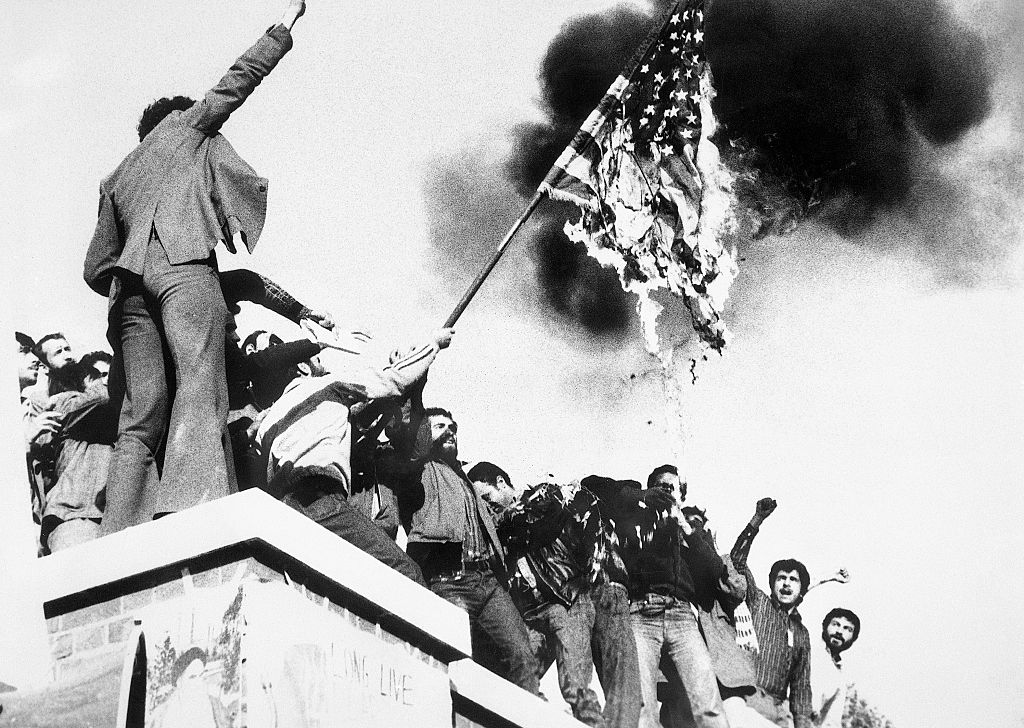 Demonstrators perched atop of the United States Embassy wall, burn an American flag, the fourth American flag to be burned since the students seized the embassy and more than 60 hostages Nov. 4th. demonstrators also burned an effigy of President Carter, Nov. 9th. (Bettmann Archive)