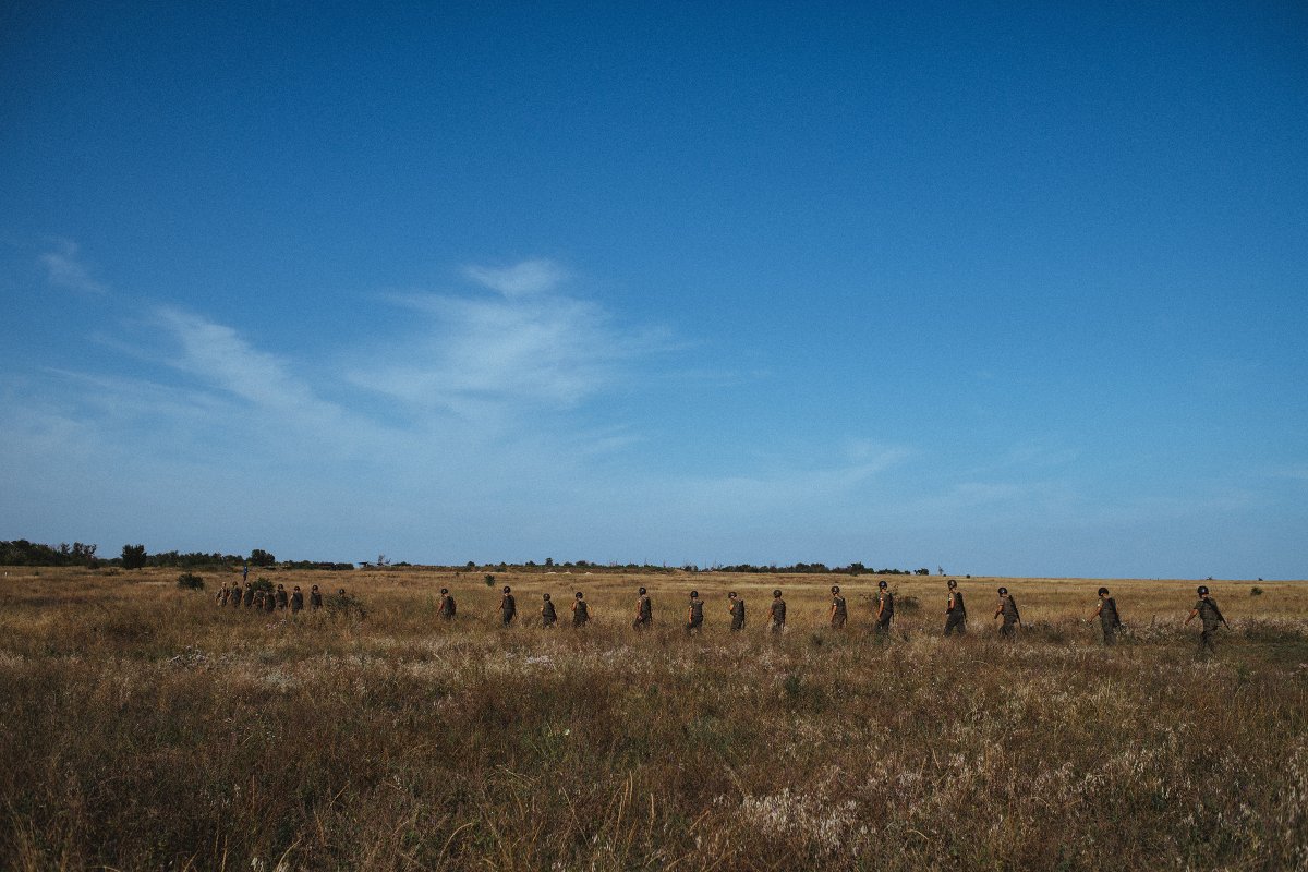 A line of new recruits walk through a field during basic training at the Azov base near Mariupol. Located near the Sea of Azov, from which the movement derives its name, the base is large enough to accommodate drills with Azov's arsenal of artillery pieces.