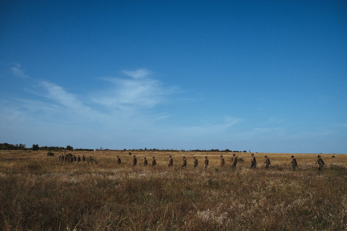 A line of new recruits walk through a field during basic trainingÂ at the Azov base near Mariupol. Located near the Sea of Azov, from which the movement derives its name, the base is large enough to accommodate drills with Azov's arsenal of artillery pieces.