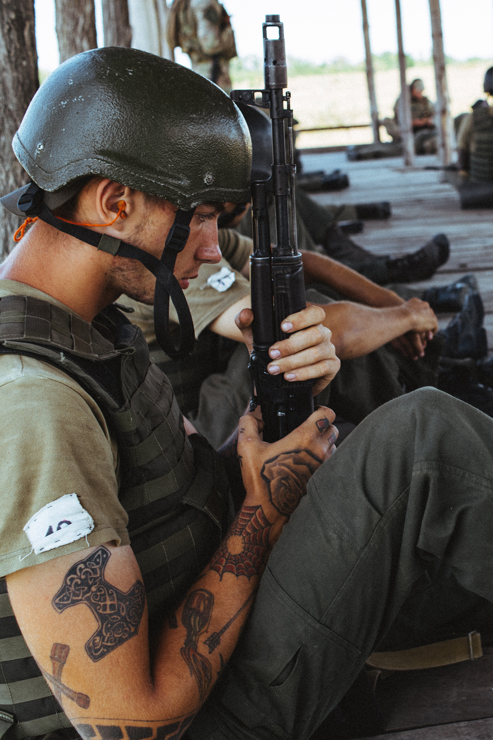 A young Azov recruit holds his rifle during basic training. His tattoos feature symbols often used by right-wing radicals around the world, including the Black Sun and Thor's Hammer.