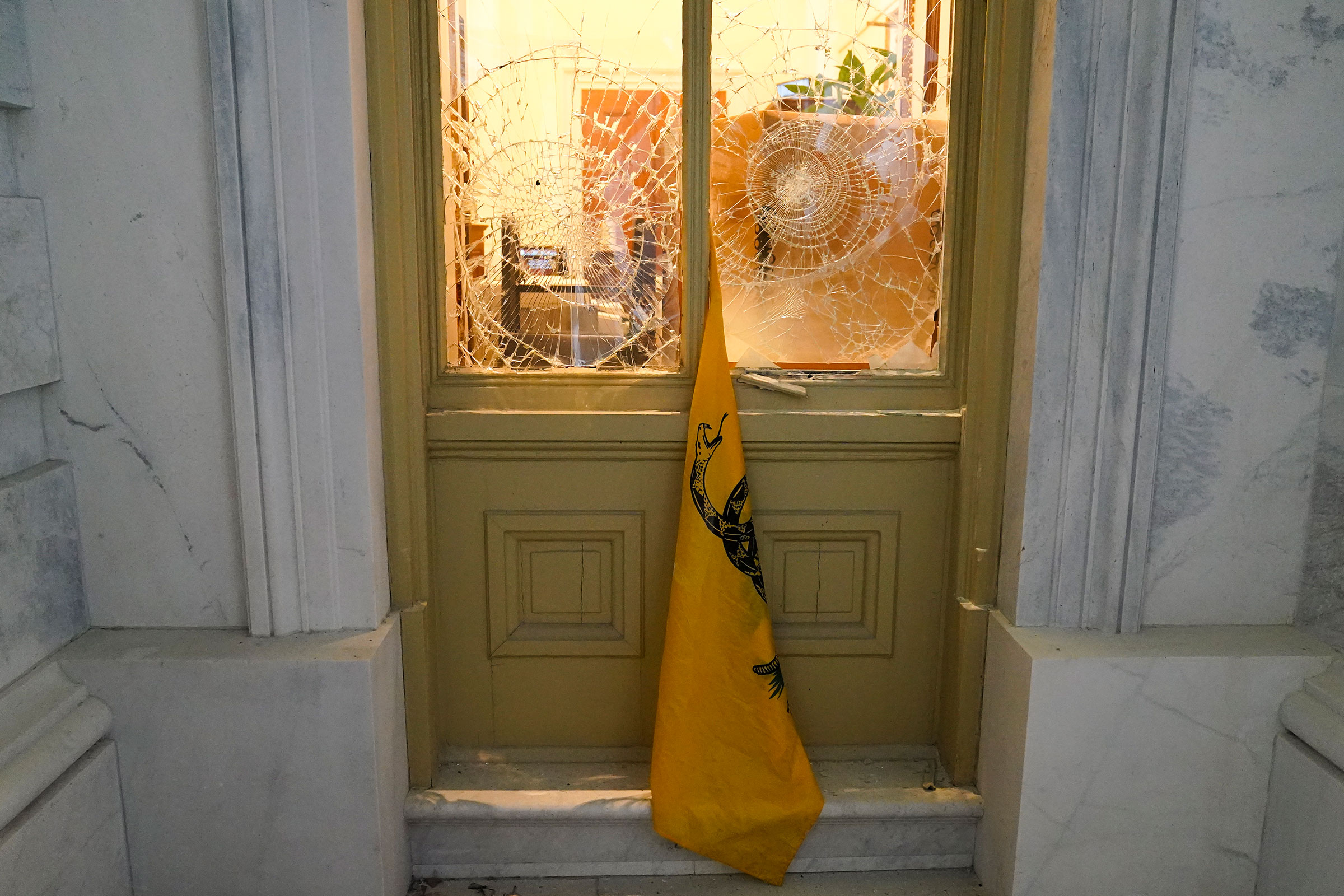 A flag hangs between broken windows after supporters of President Donald Trump tried to break through police barriers outside the Capitol on Jan 6. (John Minchillo—AP)