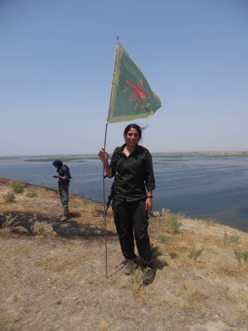 Azeema standing with flag in the Kobani countryside, January 2015