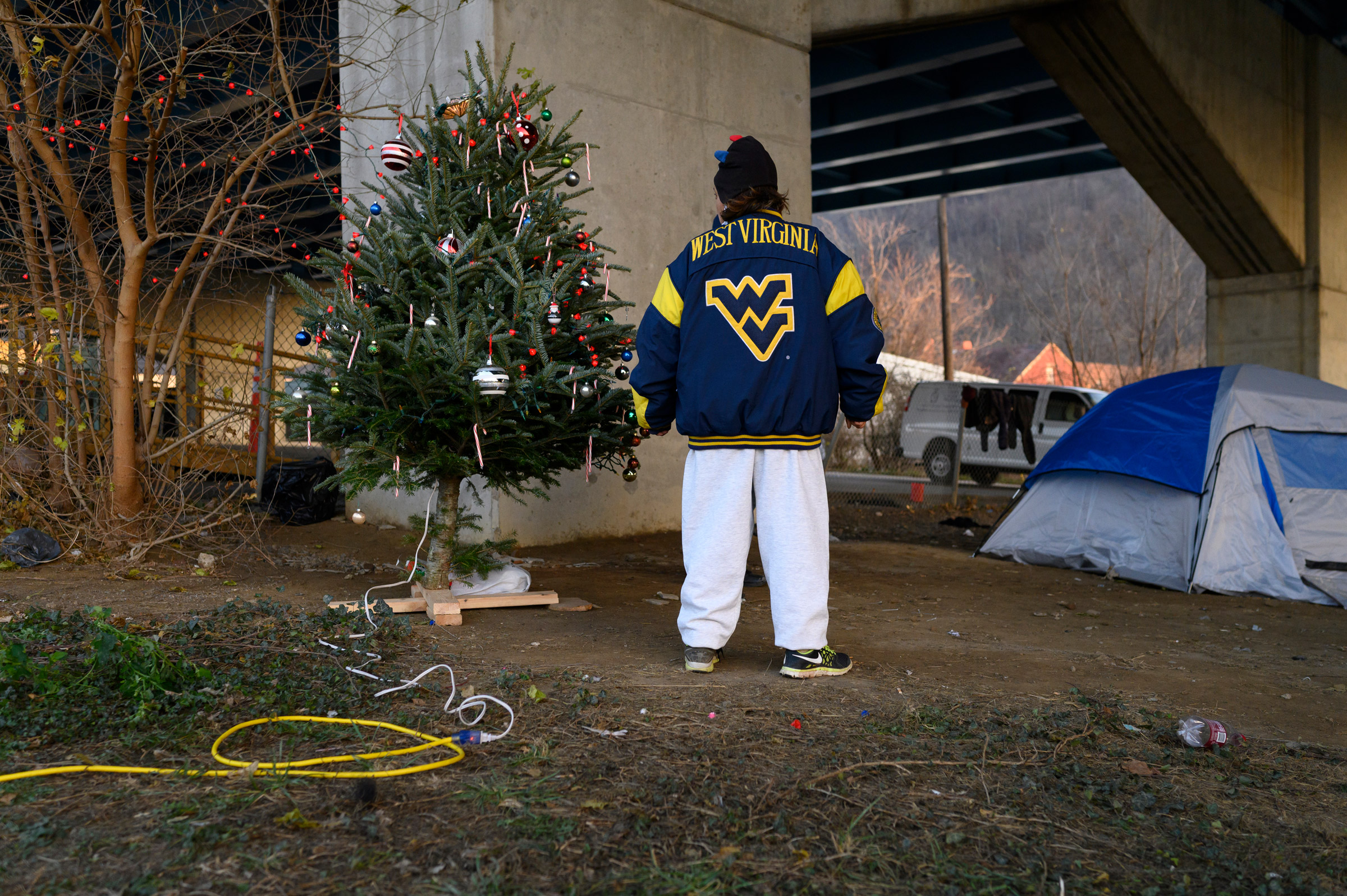 Chrissy stands by a Christmas tree in her encampment on Dec. 9. Chrissy helped bring the tree with others to hold a celebration and sing carols. After complaints, the City of Wheeling removed the tree's power, citing that they agreed to supply electricity for a temporary shower station adjacent to the camp but had not agreed to have it used for anything else. (Rebecca Kiger)