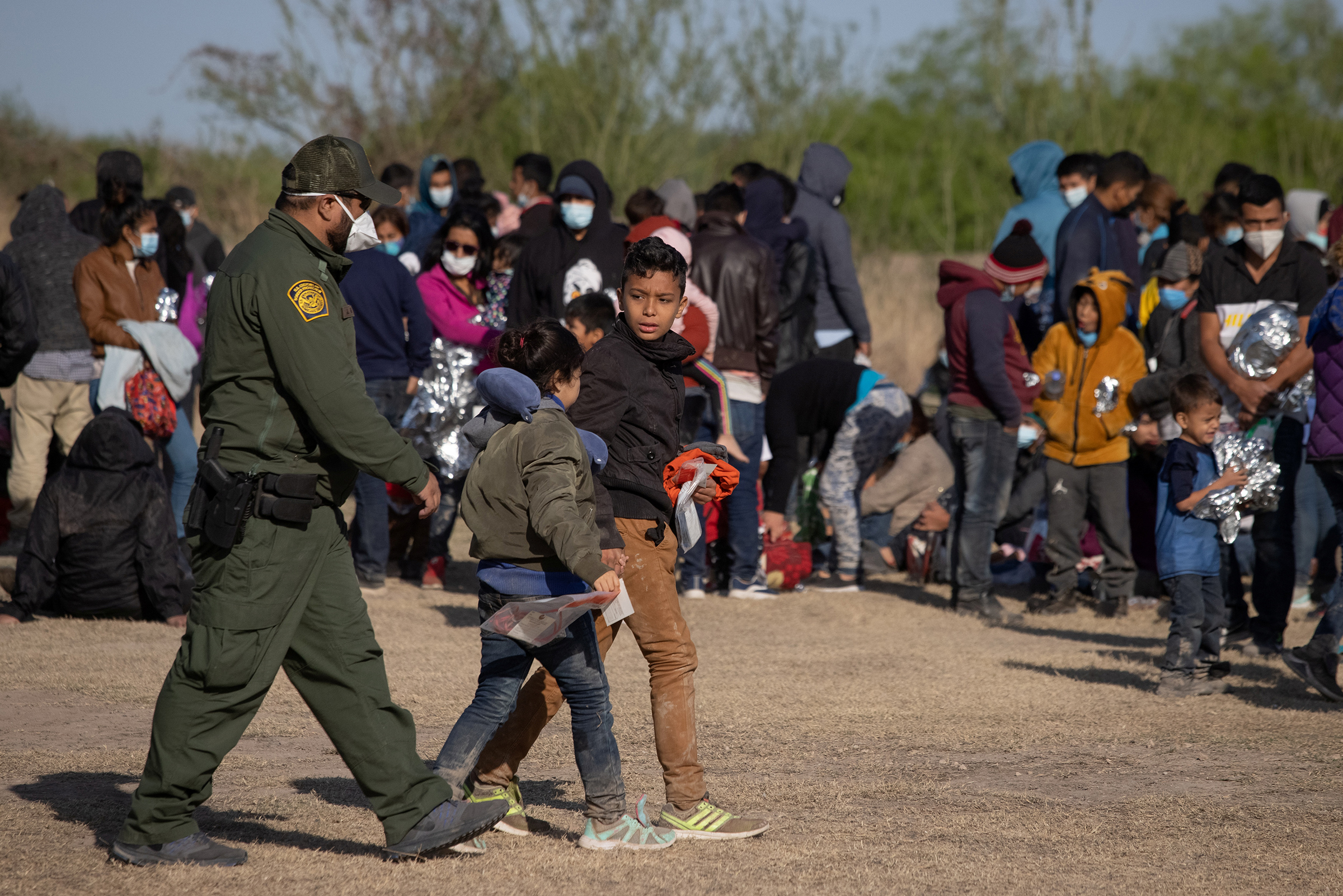 A U.S. Border Patrol Agent escorts two asylum-seeking unaccompanied minors from Central America as others take refuge near a baseball field after crossing the Rio Grande river into the United States from Mexico on rafts, in La Joya, Texas, on March 19