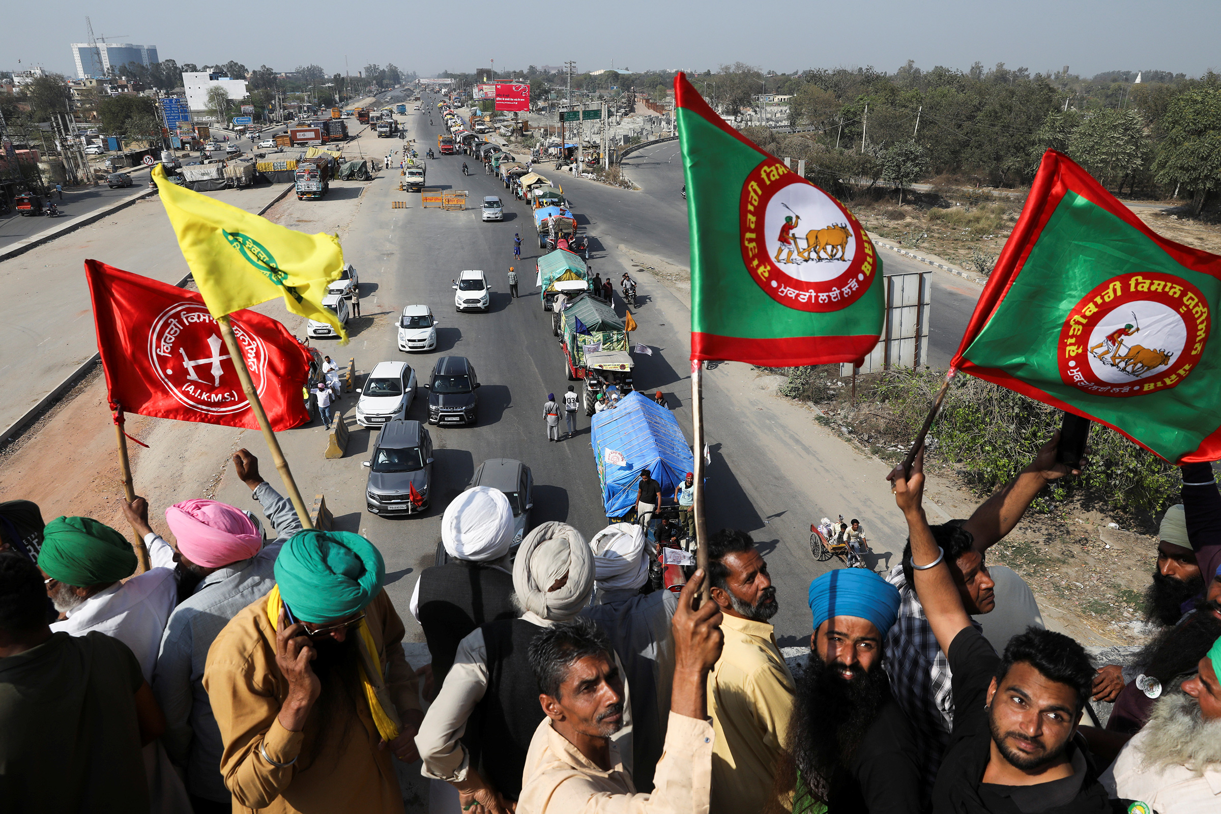 Farmers cheer and wave flags near Kundli border in Haryana, India, as more tractors arrive from Punjab to participate in the ongoing farmers' protest at Singhu border to mark the 100th day of demonstrations against the farm laws on March 6