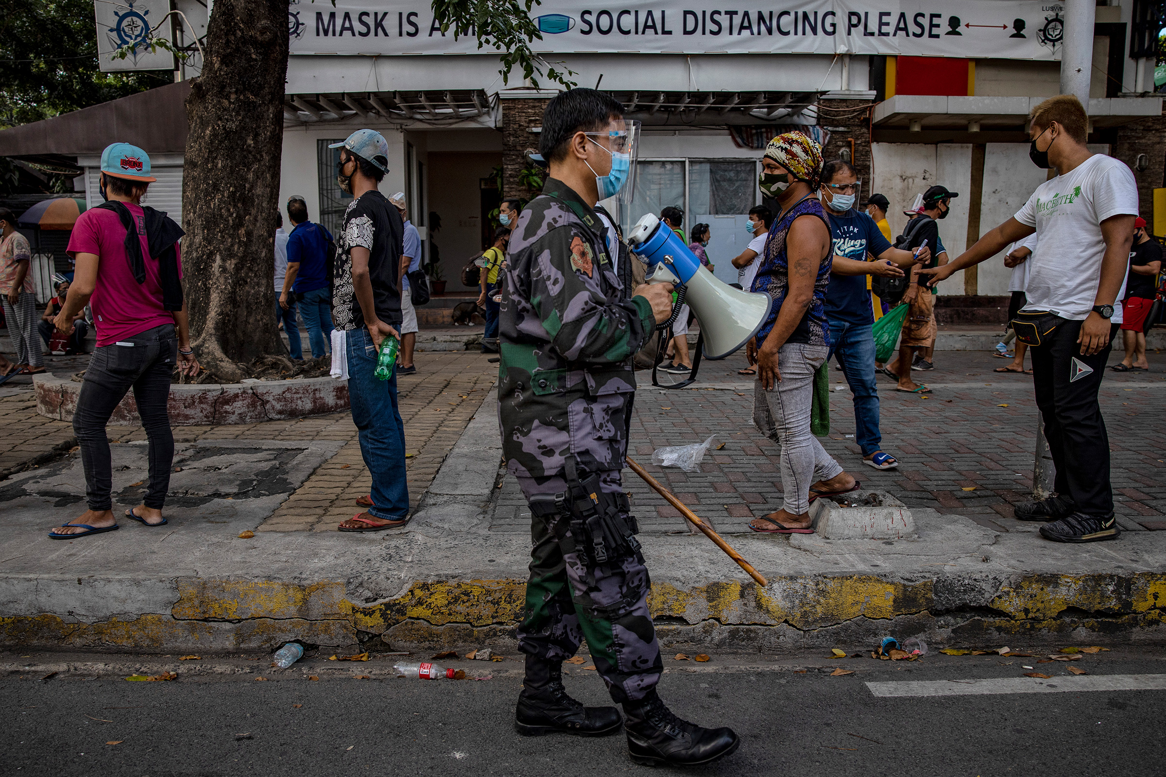 A police officer reminds homeless people to practice social distancing as they queue to receive free meals distributed by members of the Society of the Divine Word (SVD) on Dec. 15, 2020 in Manila.