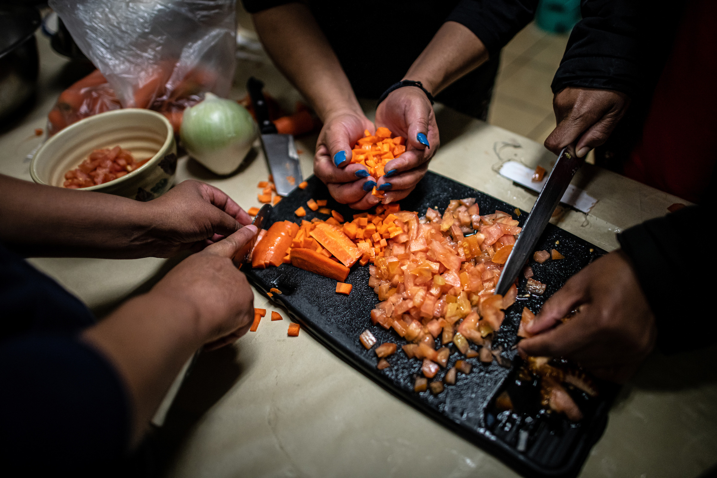 Shelter guests chop carrots while cooking soup together in the kitchen.
