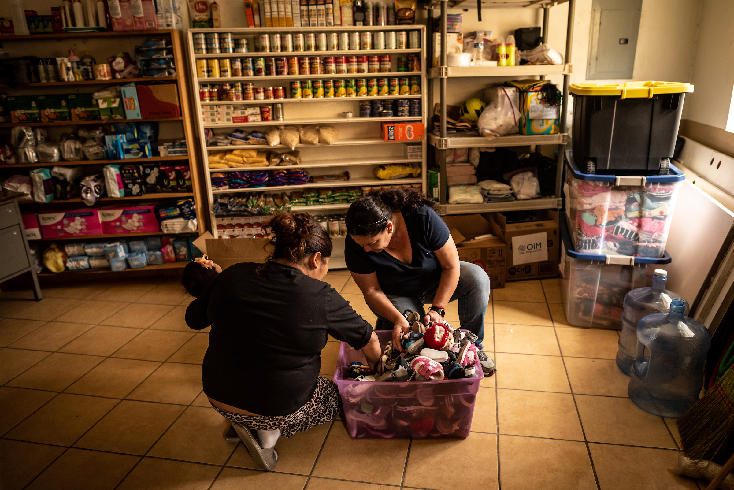 Shelter volunteer Marta Leticia Galarza Gandara, right, helps Isa find shoes for her baby daughter in a box of donations. Isa is an asylum seeker from Honduras, and has been waiting at the border under MPP since September 2019.