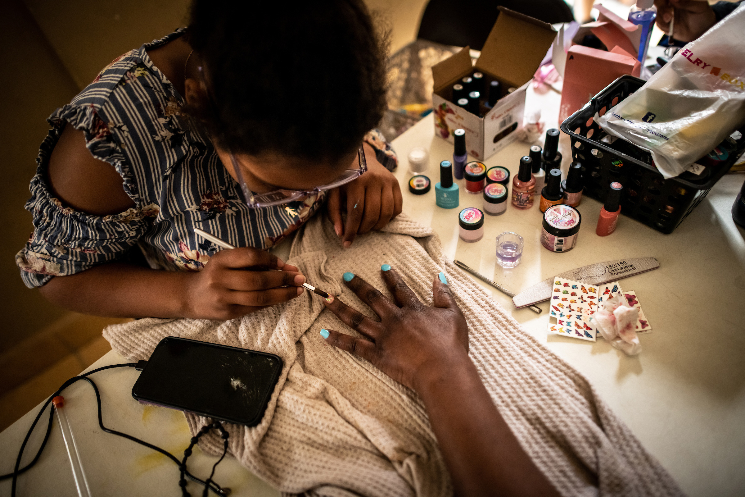 Migrants give each other gel manicures. Manicuring is one of the most accessible jobs migrant women can attain to earn an income in Ciudad Juárez. The shelter funds some women to get professional training, and then they share what they've learned by training other women at the shelter.