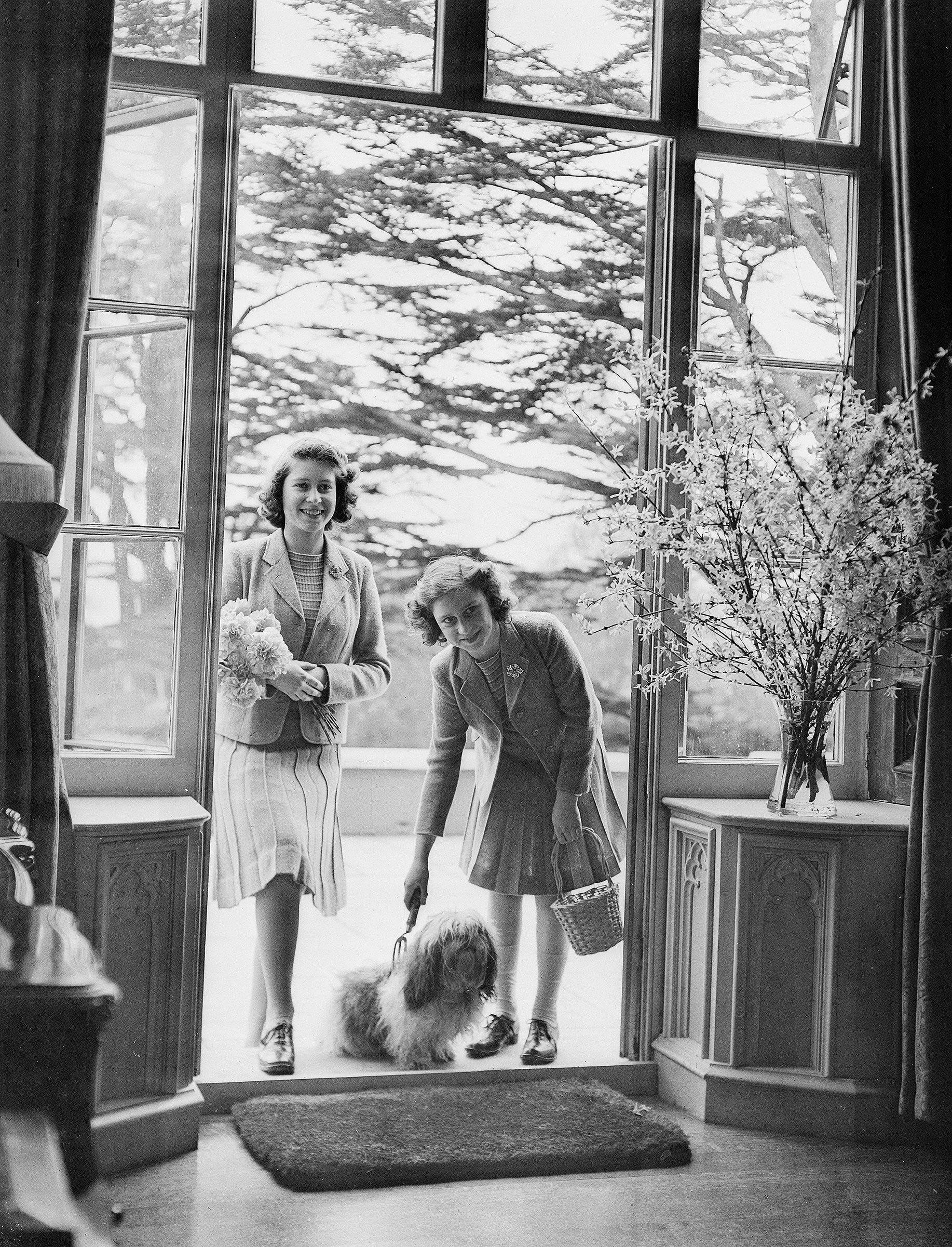 Princess Elizabeth and Princess Margaret stand in a doorway with a pet dog at the Royal Lodge in Windsor Castle, England on April 11, 1942. (Studio Lisa/Getty Images)
