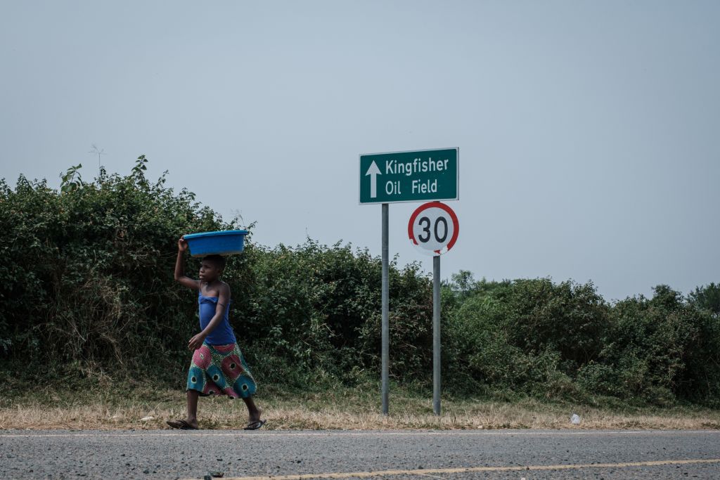 A girl walks past a sign for the Kingfisher oil field in the south-east of lake Albert in Uganda, on Jan. 24, 2020 (Yasuyoshi Chiba—AFP via Getty Images)