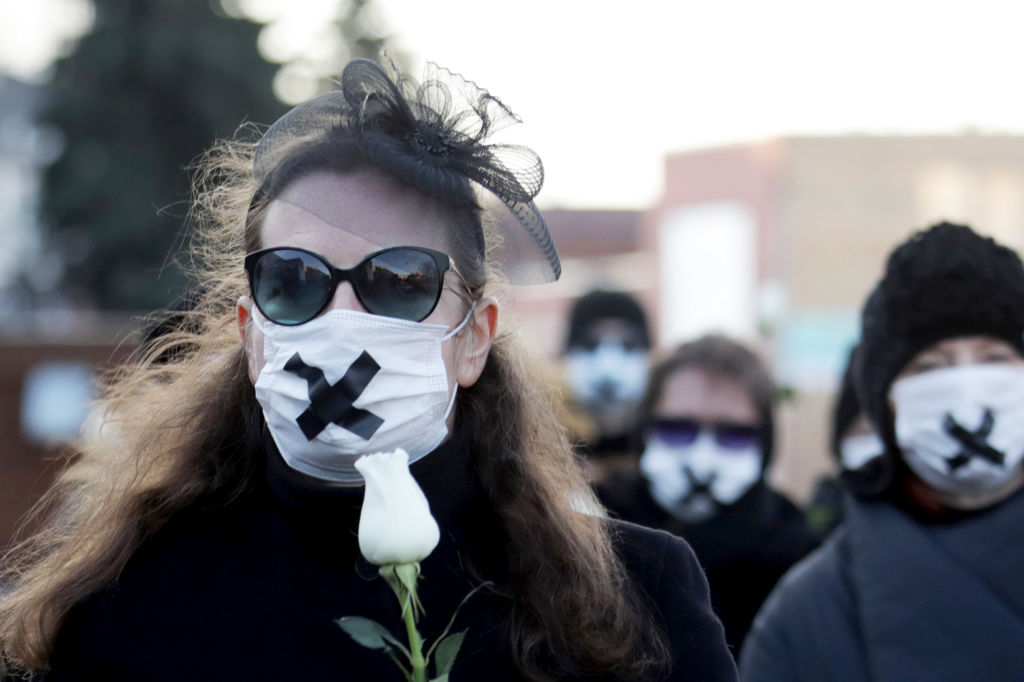 Women wearing black clothing and tape crossed over their mouths hold white roses as they march on March 2, 2021, in Minsk, during a demonstration against the conviction of a doctor and a journalist over the disclosure of medical records of a protester who died after being detained at one of the post-election rallies that swept Belarus last year. (AFP via Getty Images)