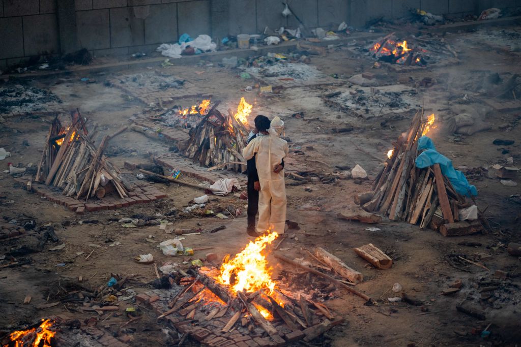 Family members embrace amid burning pyres of people who died due to COVID-19 at a cremation ground in New Delhi on April 26, 2021.