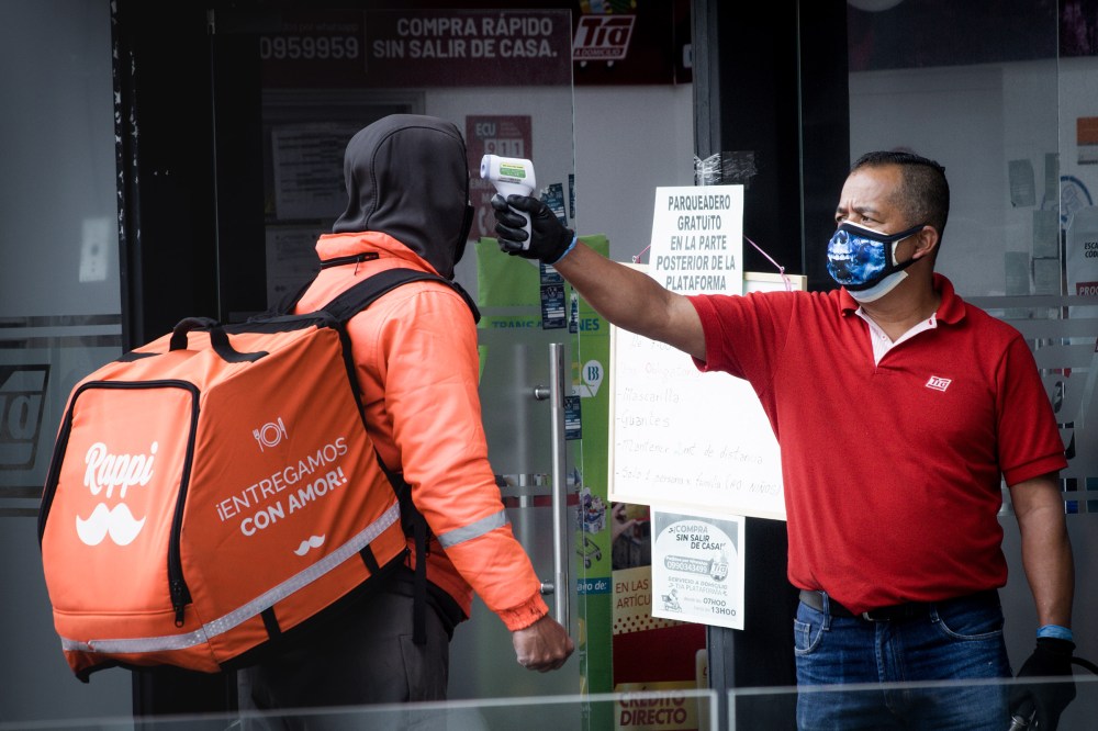 A market store guard messearues the temperature of a delivery driver in Quito, Ecuador. During the city lockdown imposed by the government to prevent the spread of Covid-19.