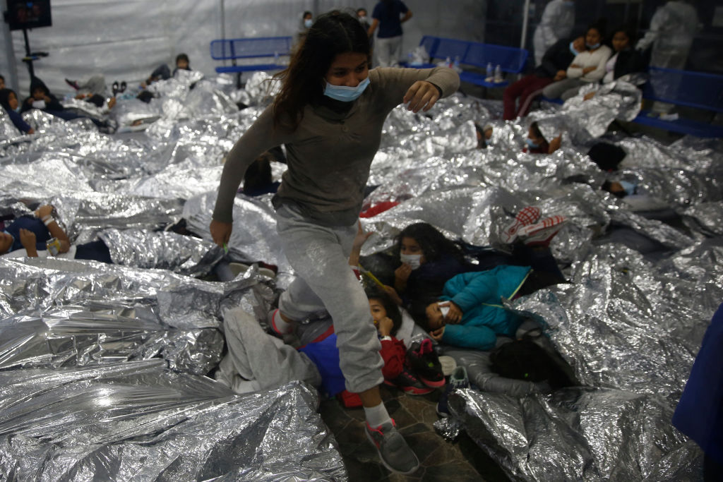 A young girl walks over others as they lie inside a pod for females at the Department of Homeland Security holding facility in Donna, Texas. (Photo by Dario Lopez-Mills / POOL / AFP)