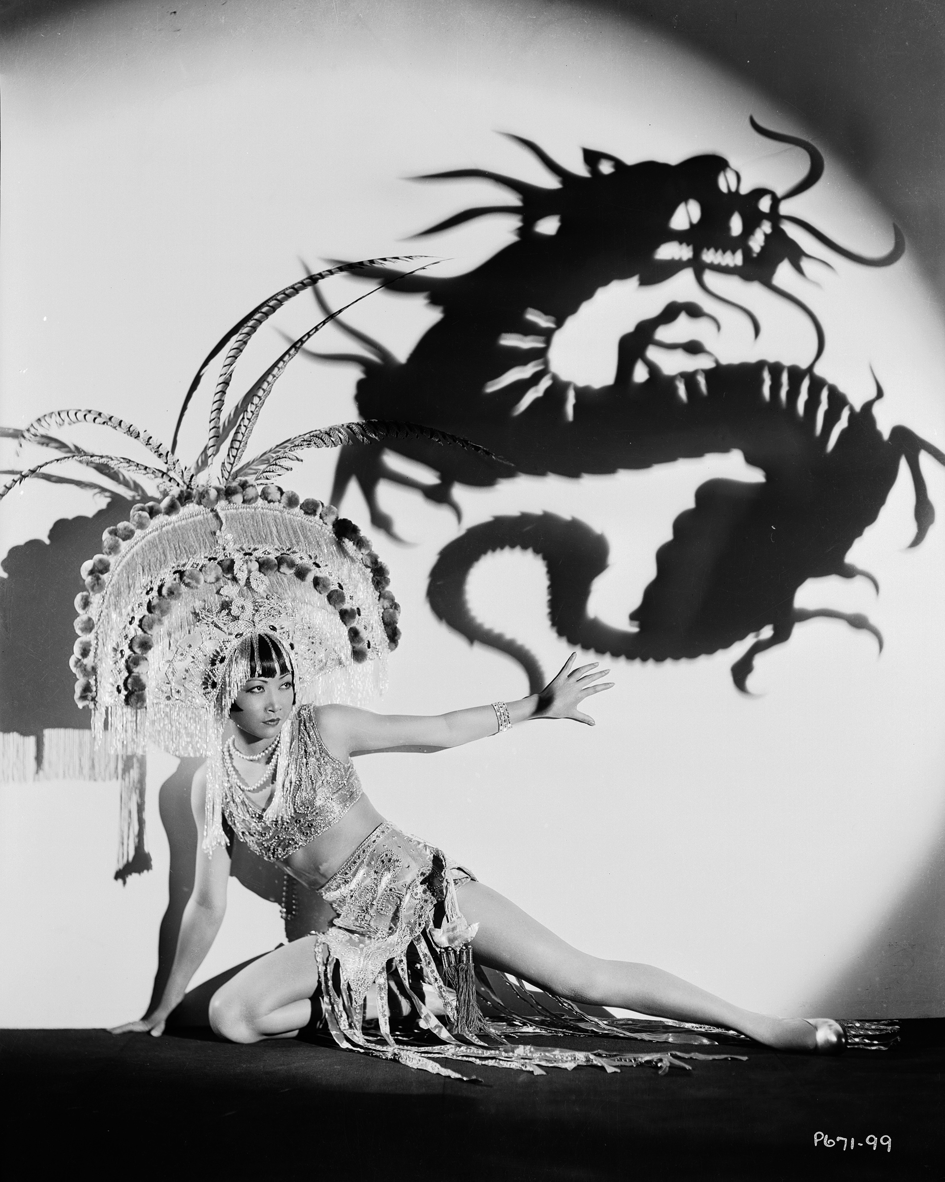 Chinese-American film star Anna May Wong wearing an exotic costume and headdress, circa 1931. Above her is a projected shadow of a dragon.