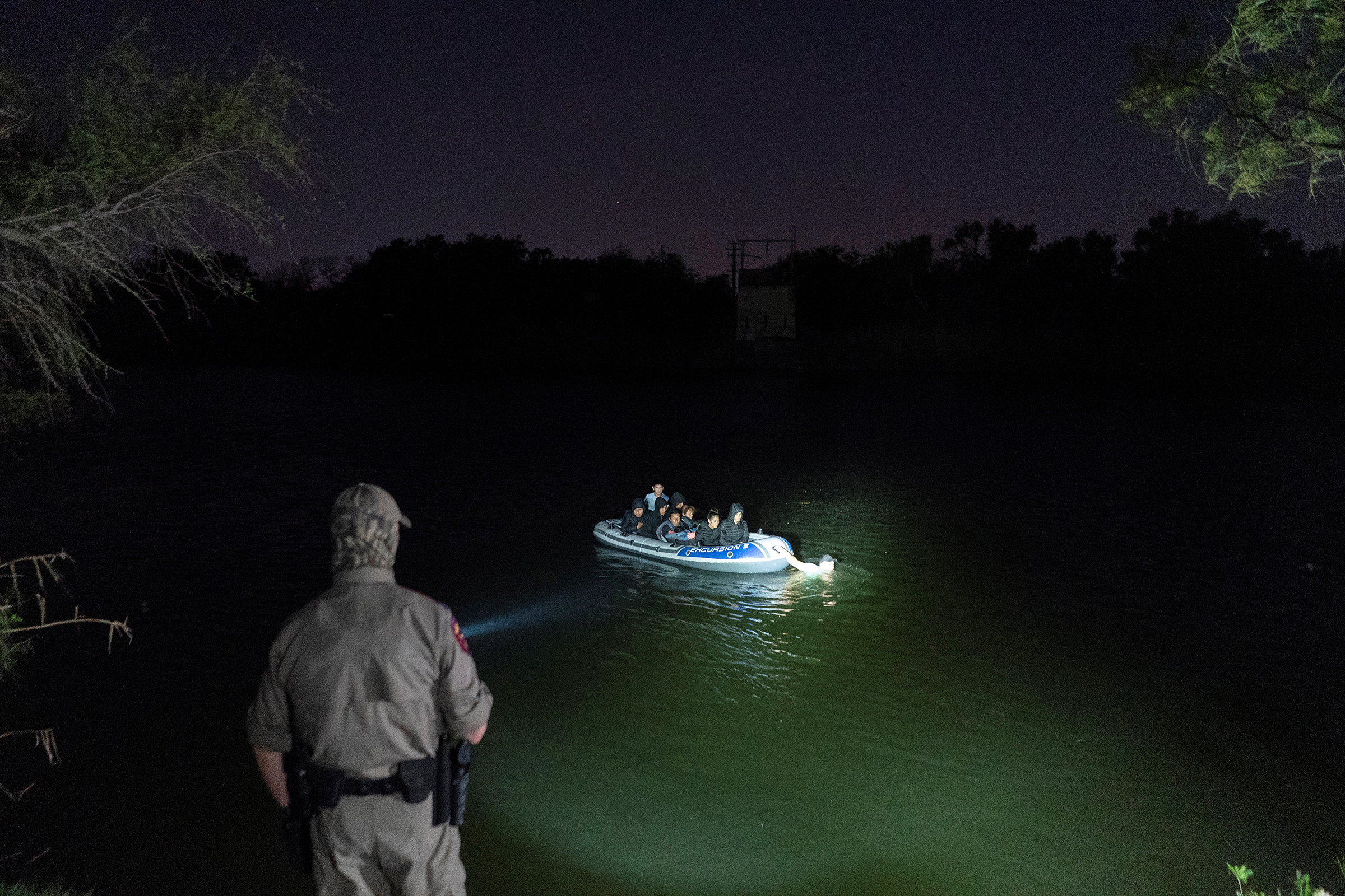 Asylum-seeking migrants' families cross the Rio Grande from Mexico as a Texas State Trooper officer points a flashlight at the inflatable raft in Roma, Texas, on April 8, 2021. The raft later turned back to the Mexican side and did not land on the U.S. side of the river. (Go Nakamura—Reuters)