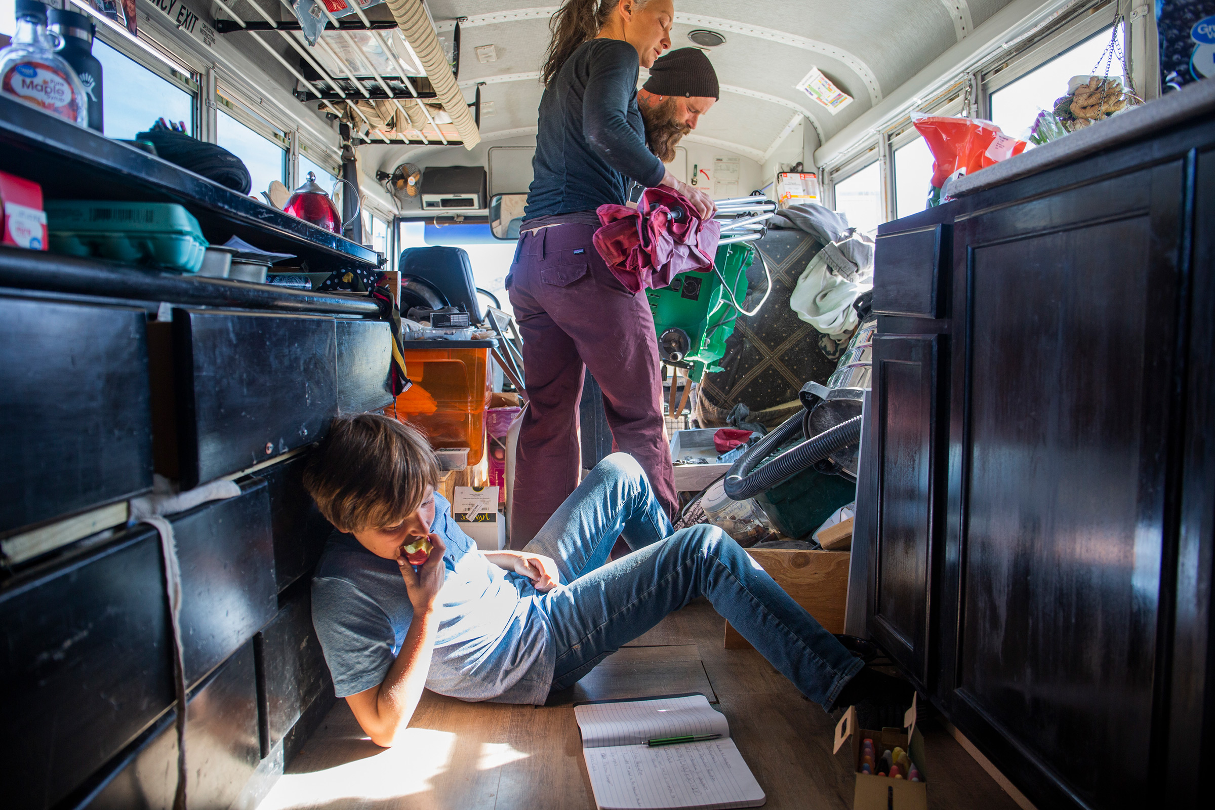 Max works on chemistry schoolwork on the floor of the bus, while Paula lends her table saw to a neighbor to work on his own bus on Feb. 23.