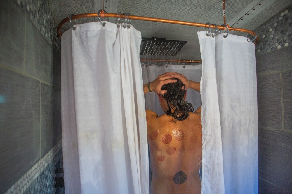 Paula showers in her handmade bathroom on the school bus, which includes a compost toilet and bathtub made from a metal trough. She suffered a major back injury years ago, and the bruising on her back is from â€˜cupping,â€™ a form of alternative medicine often used to treat muscle pain, which she lets Max practice on her when she is stressed.