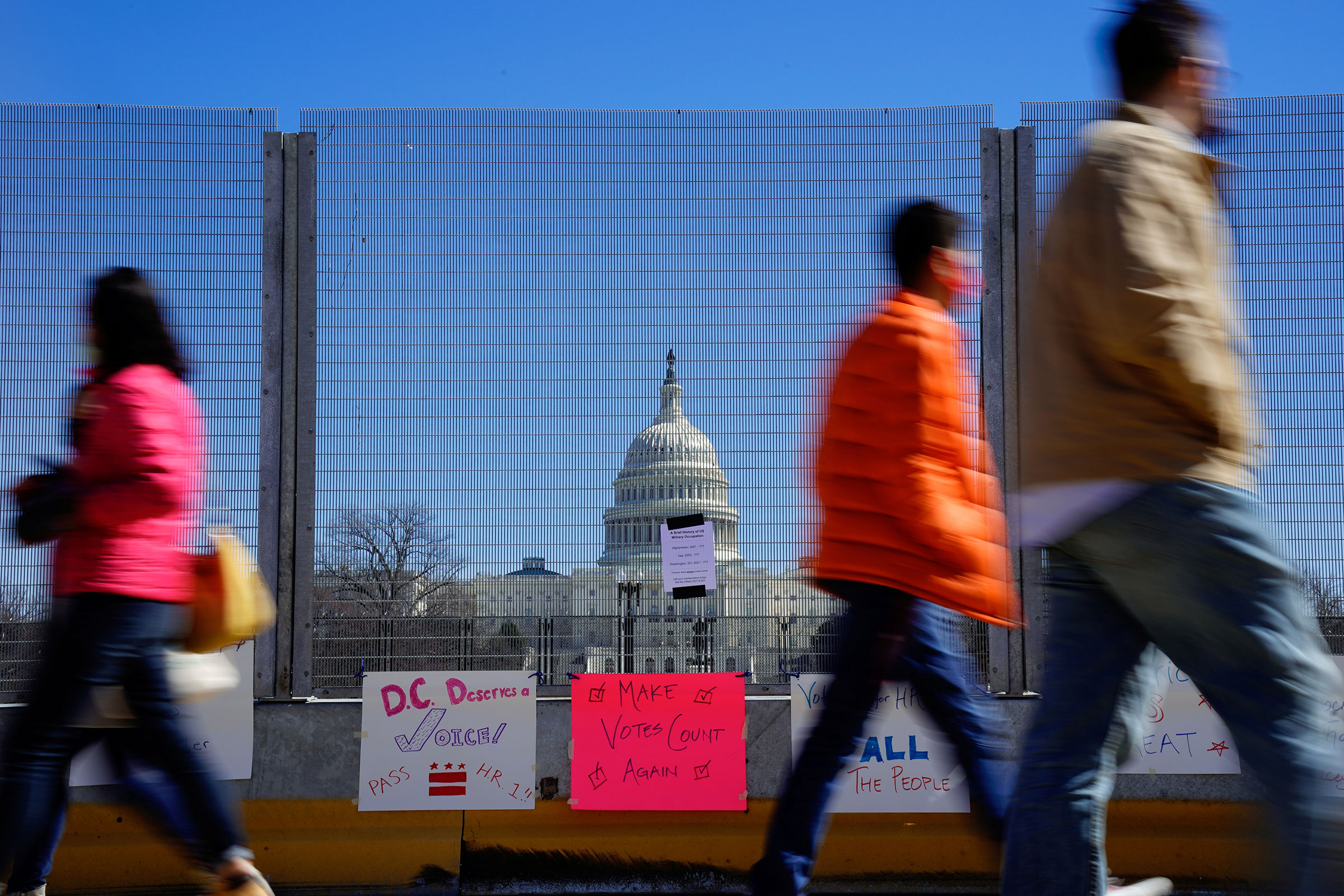 People walk past signs hung on a security fence in support of expanded voting rights near the Capitol in Washington, on March 7, 2021. (Erin Scott—Reuters)